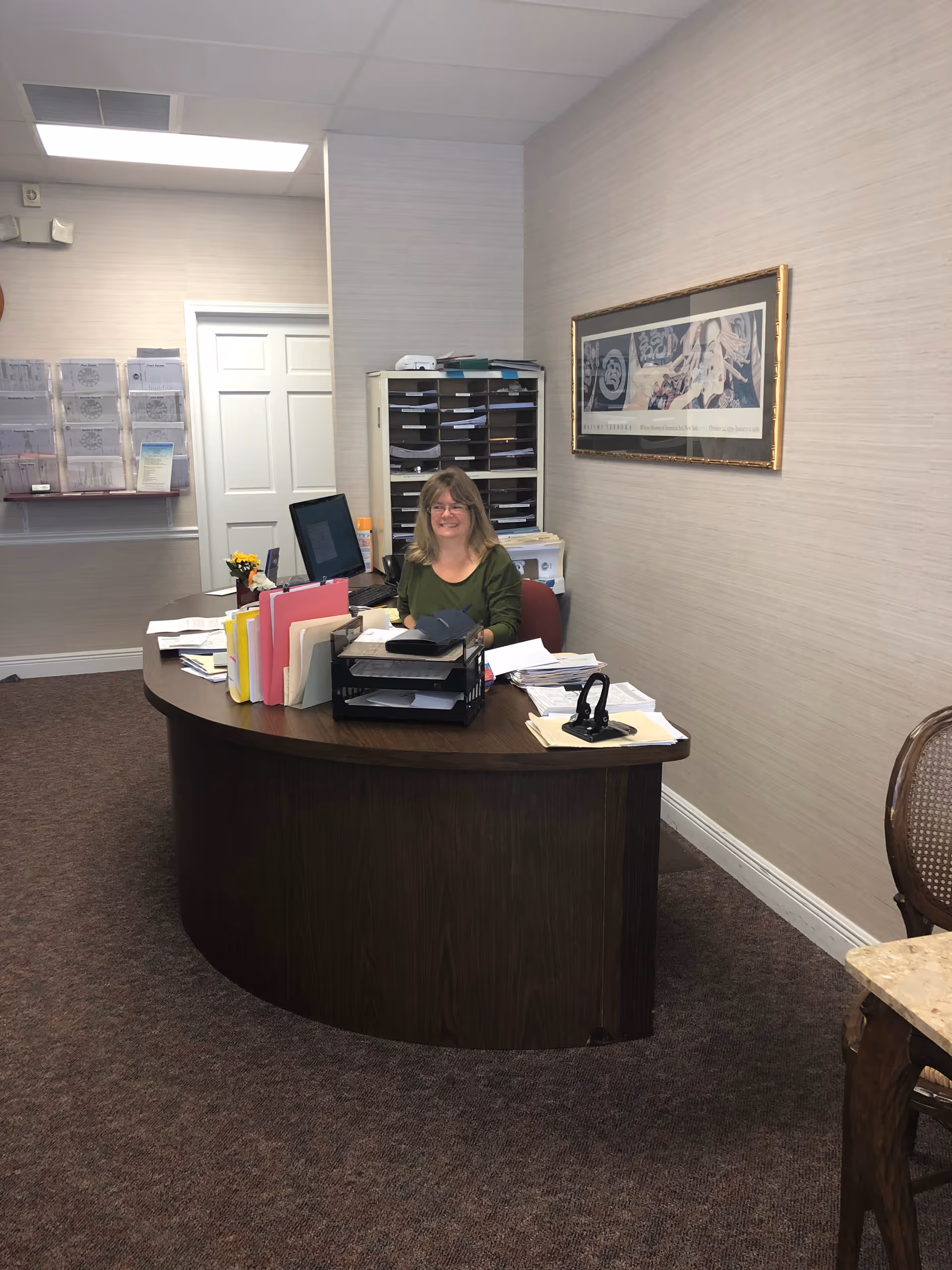 Receptionist seated at a curved desk with papers and computer in an office.