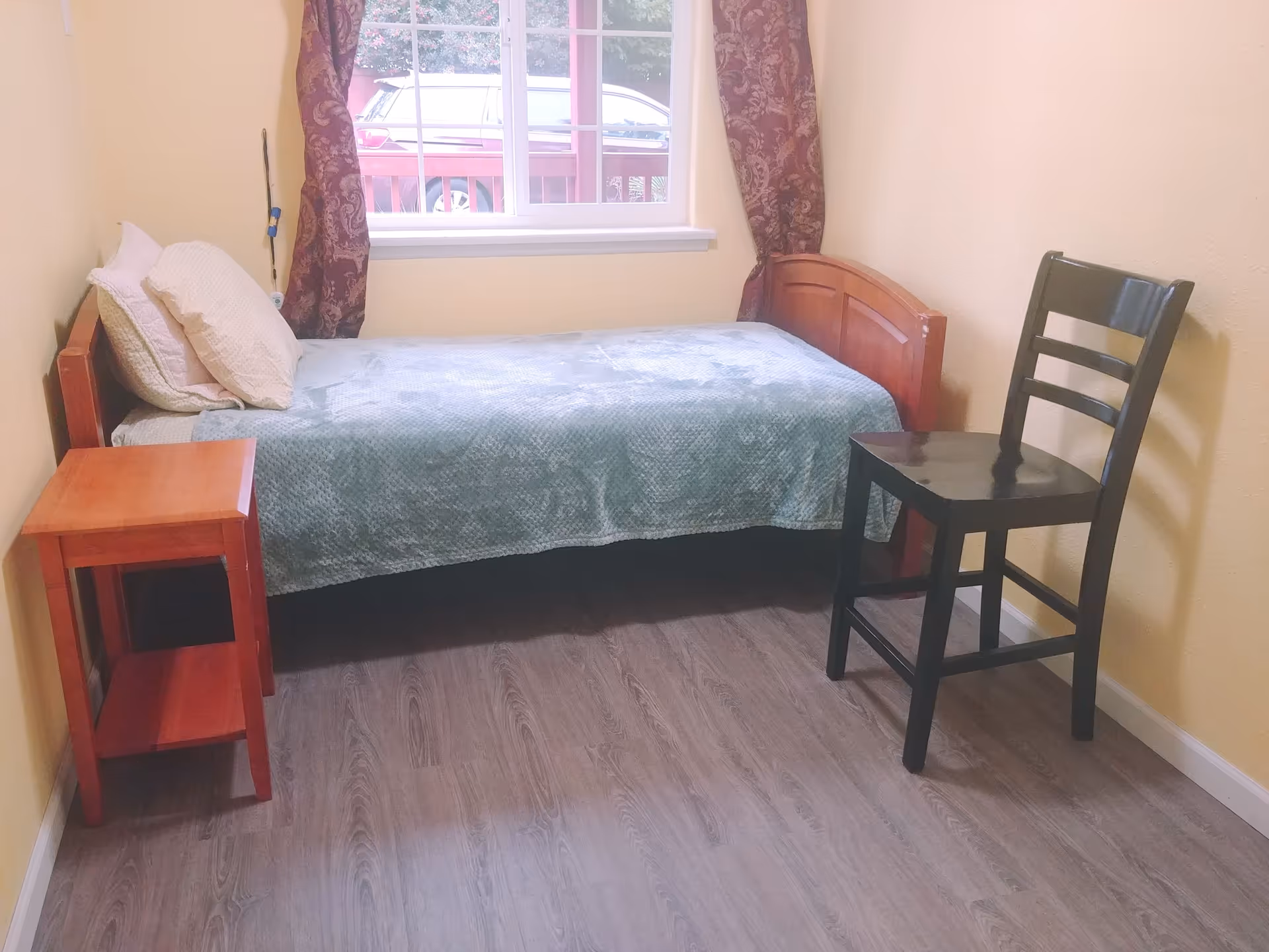 Small bedroom with a bed, nightstand, chair, window, and yellow walls.