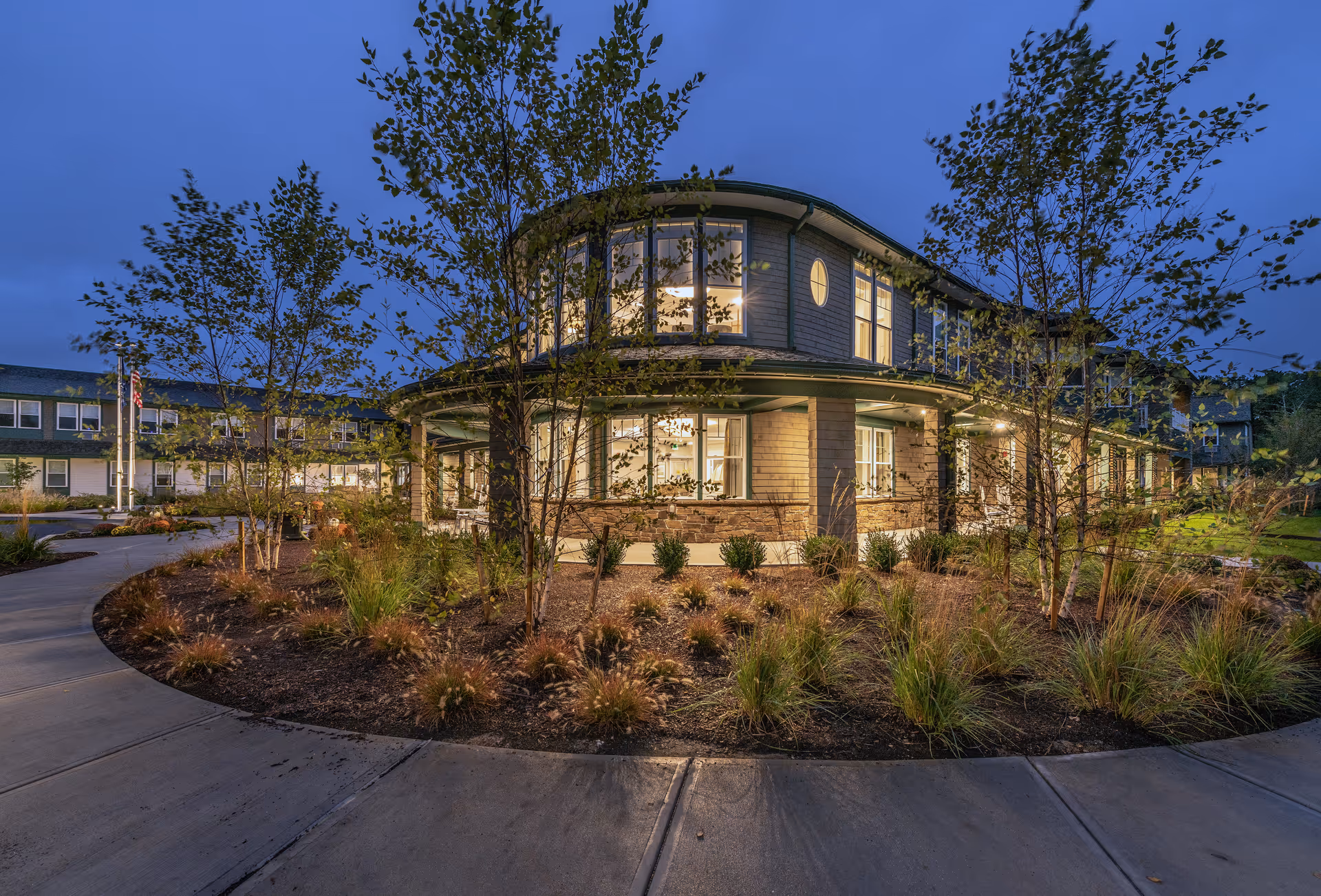 Exterior view of Laurentide at Mashpee Commons, illuminated entry with landscaped roundabout and trees.