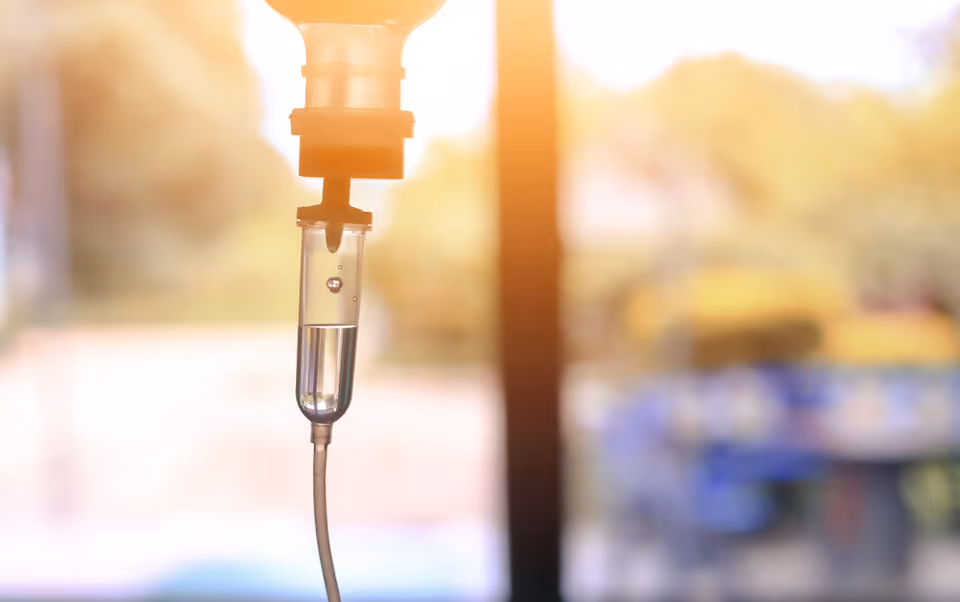 Close-up of an IV drip with a sunlit blurred background.