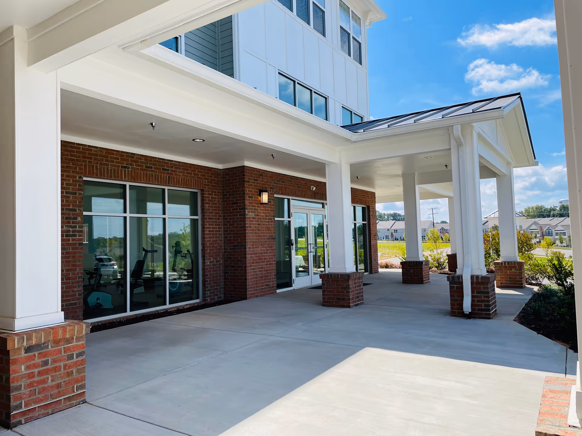 Brick and white-columned entrance with glass doors, concrete patio, and clear blue sky.