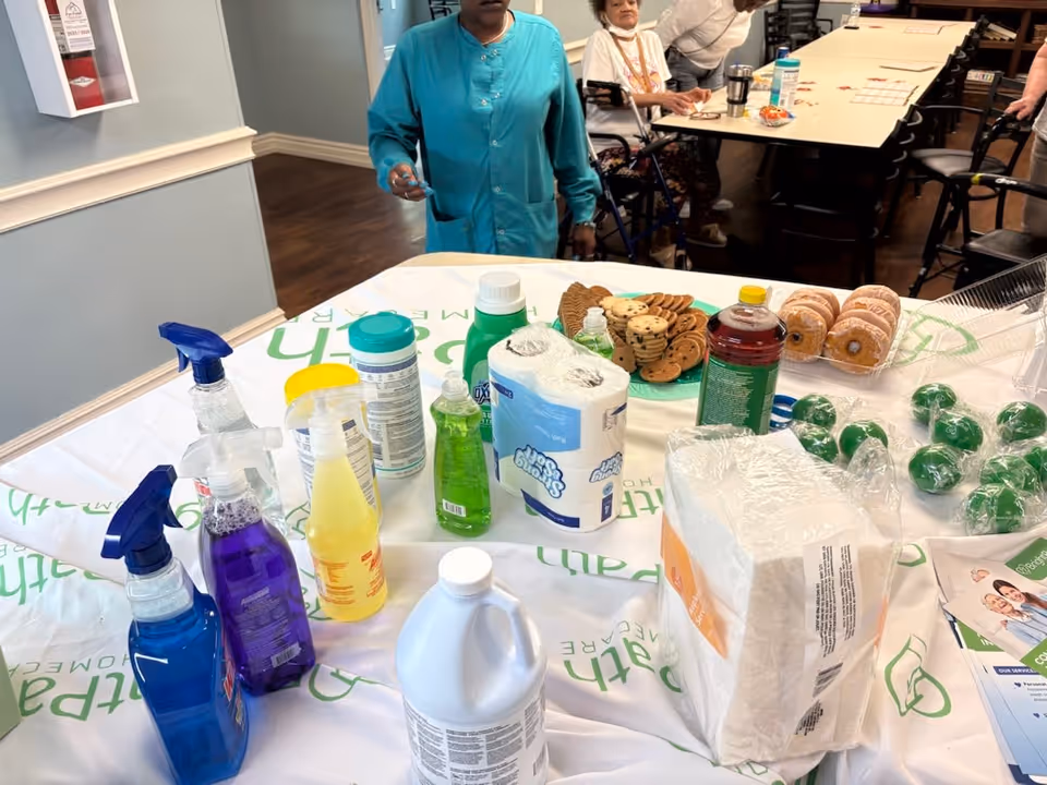 Staff and residents gather in a dining area with donuts, drinks, and cleaning supplies on table.