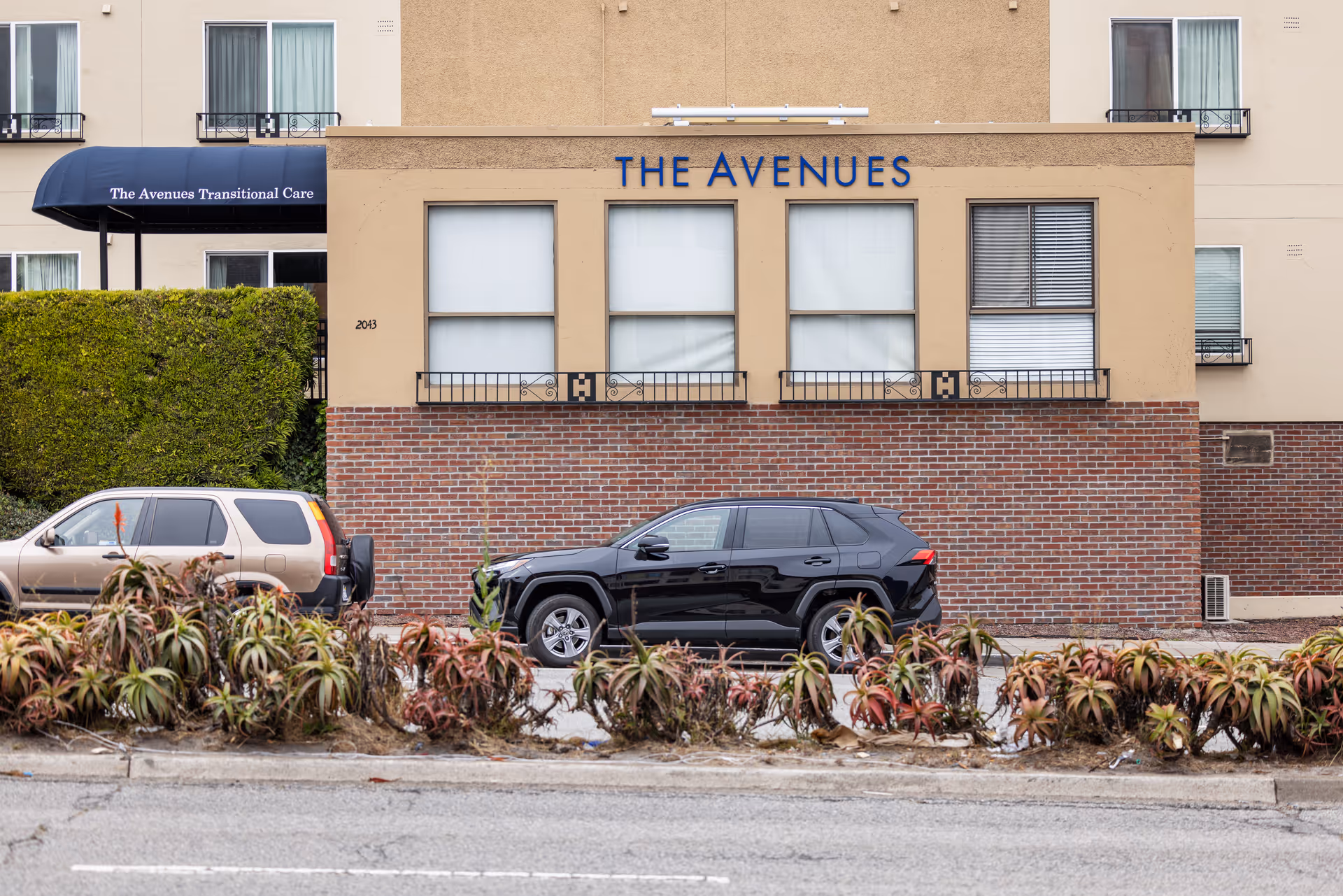 The Avenues Transitional Care Center facade with two parked cars and landscaped foreground.
