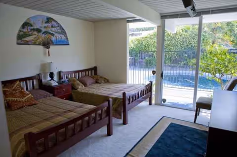 Bright bedroom with two wooden beds, nightstand, and sliding glass door to a balcony overlooking outdoors.
