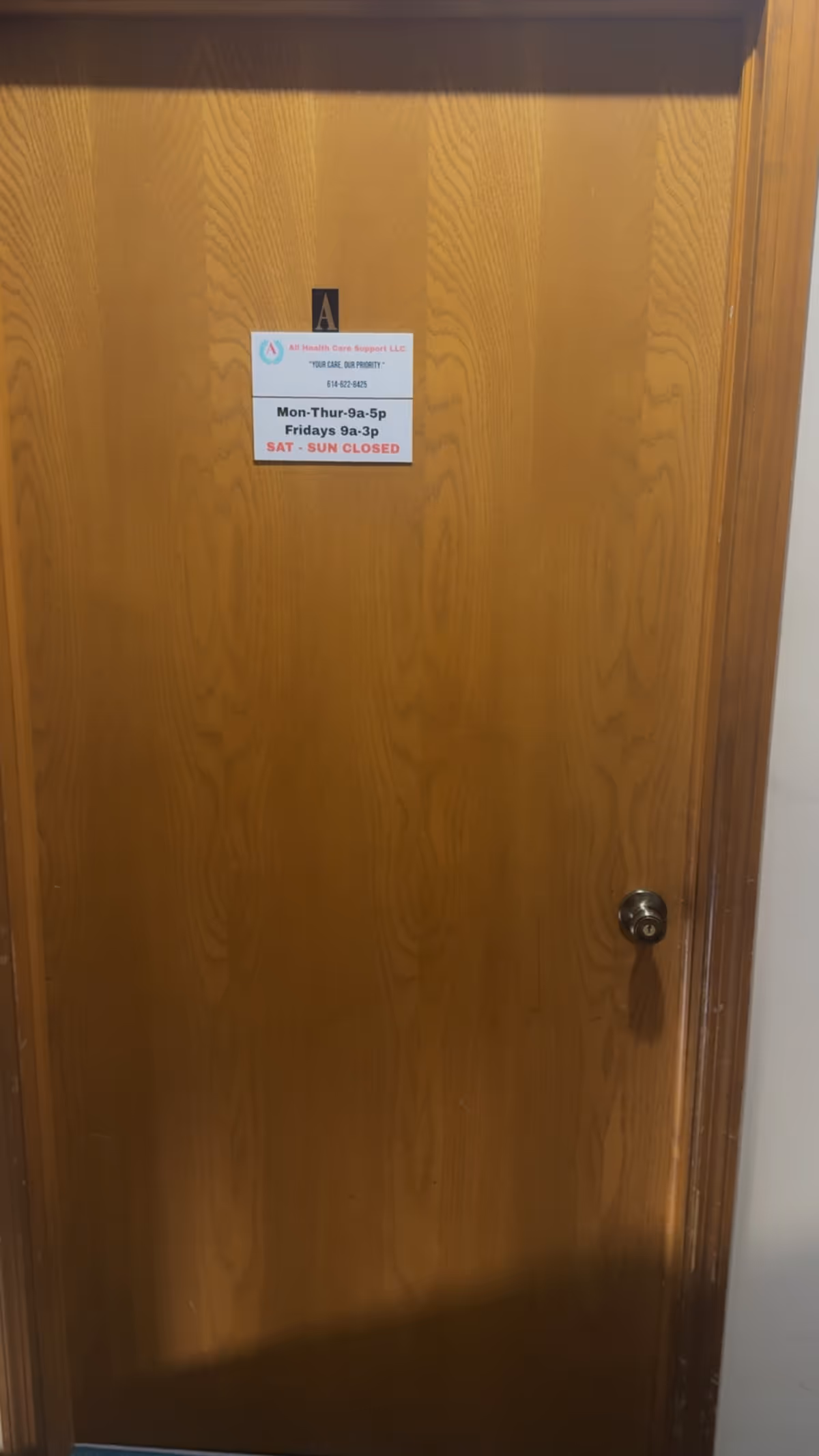 Wooden interior door with a white sign listing hours and contact info.