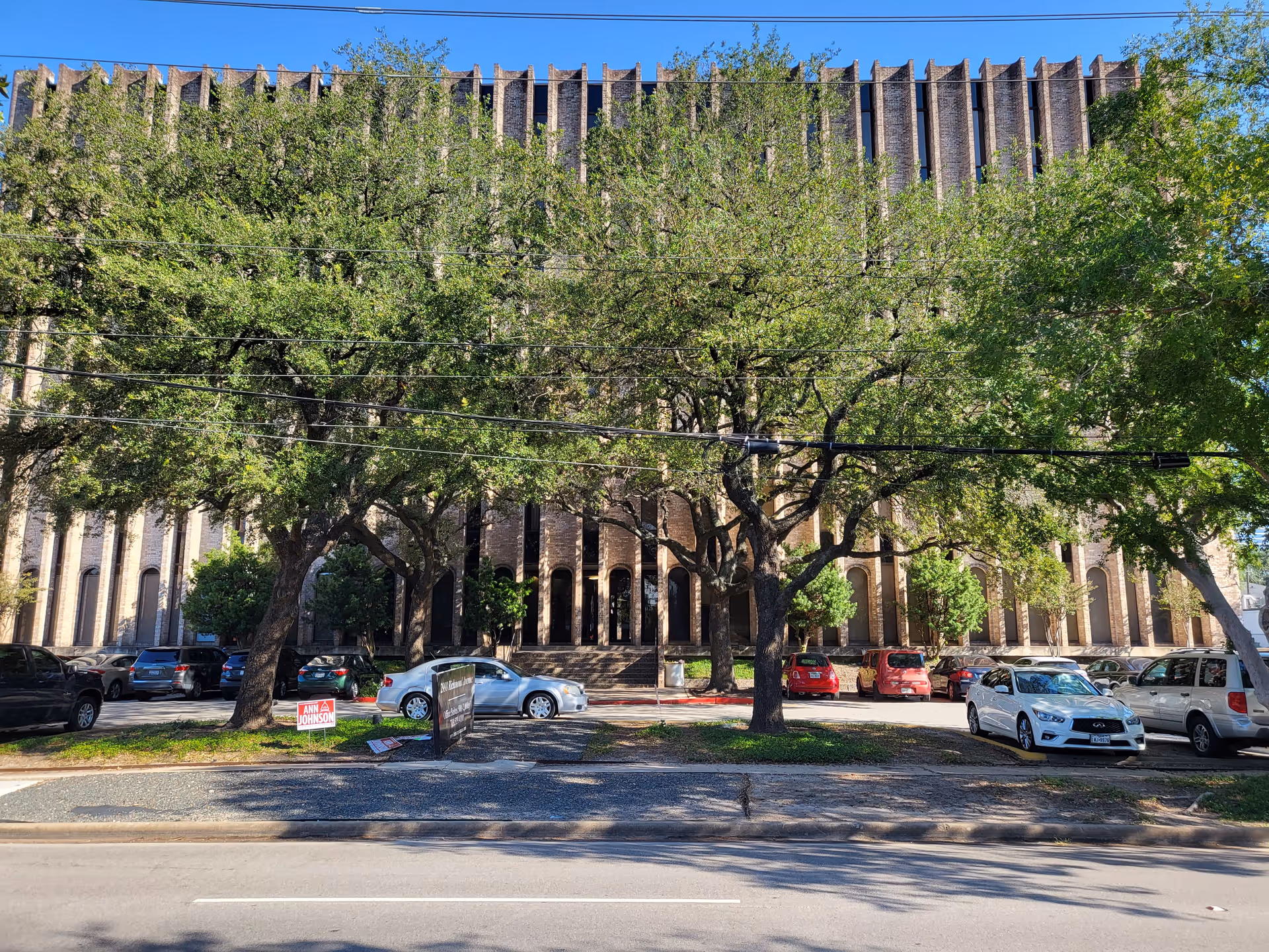 Exterior view of a brick building with tall columns, trees, and parked cars.