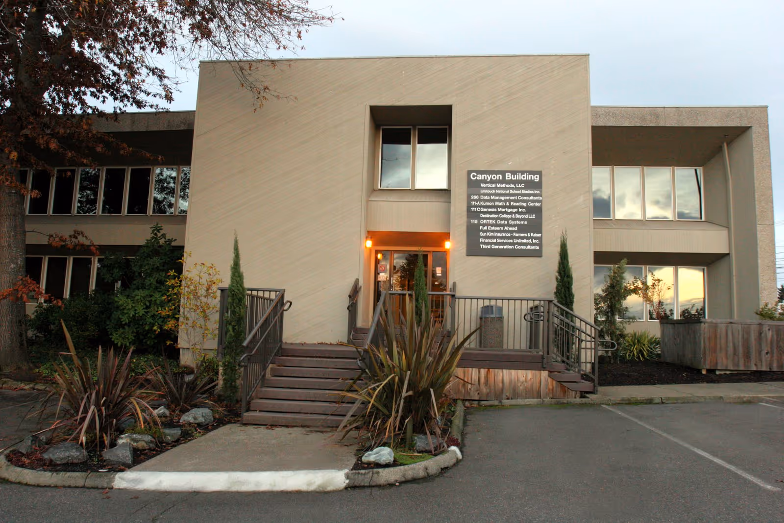 Beige two-story office-style building with steps, central entrance, and a sign