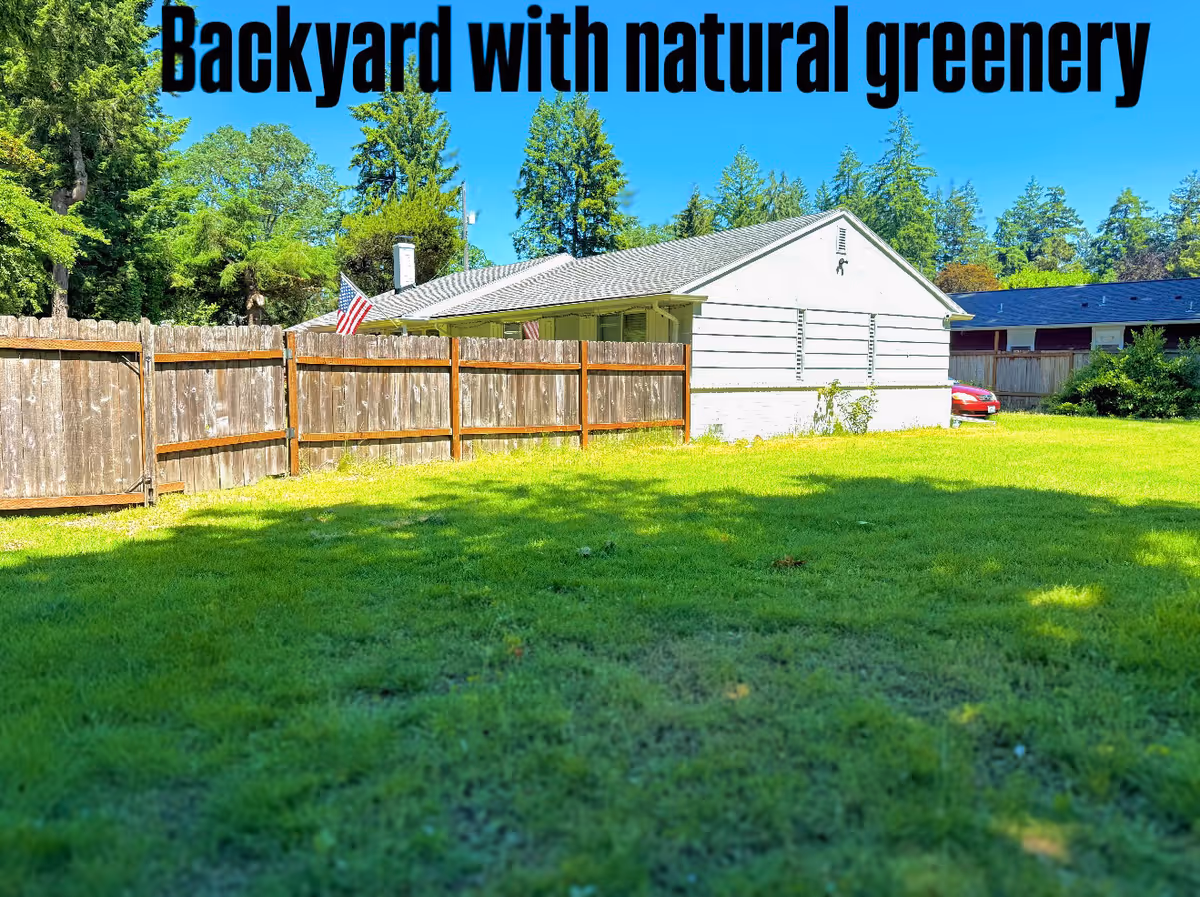 Green grassy backyard with a white single-story building and wooden fence.