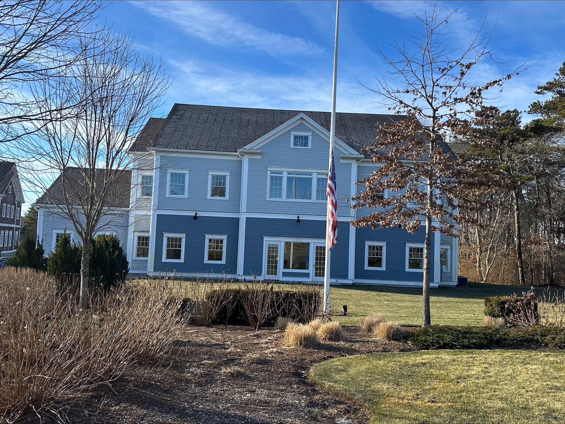 Blue multi-story senior living facility exterior with flagpole and trimmed lawn.