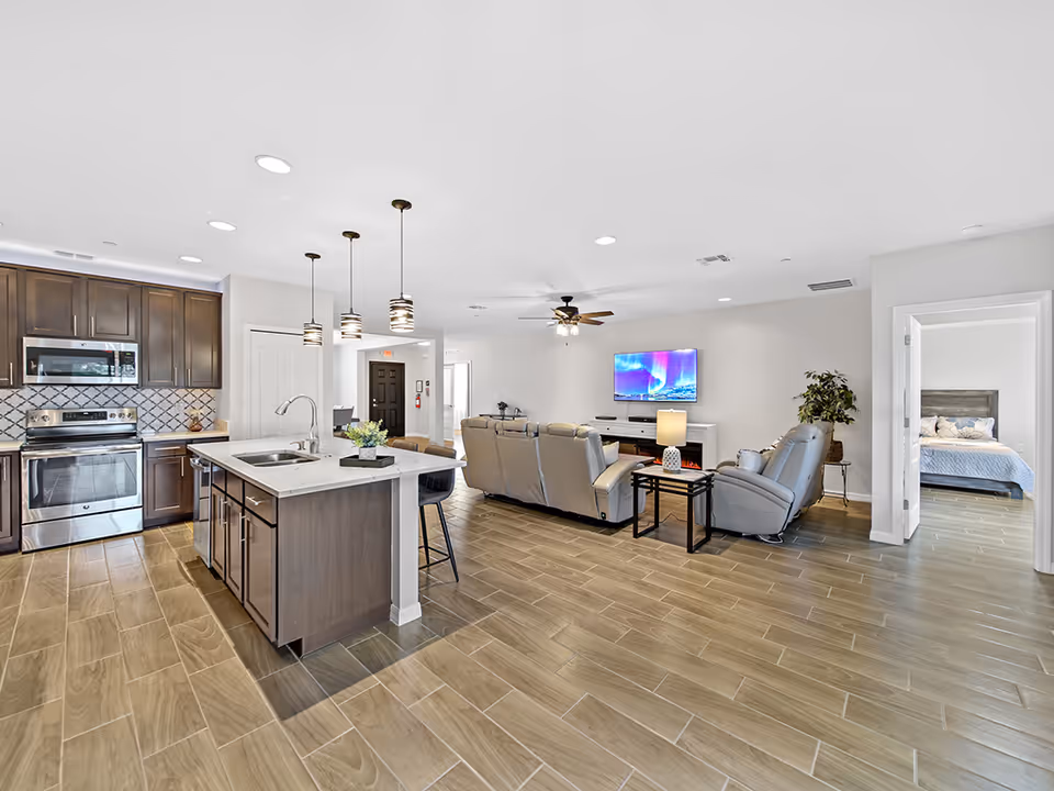 Open-concept living area with kitchen island, modern seating, TV, and a bedroom doorway.