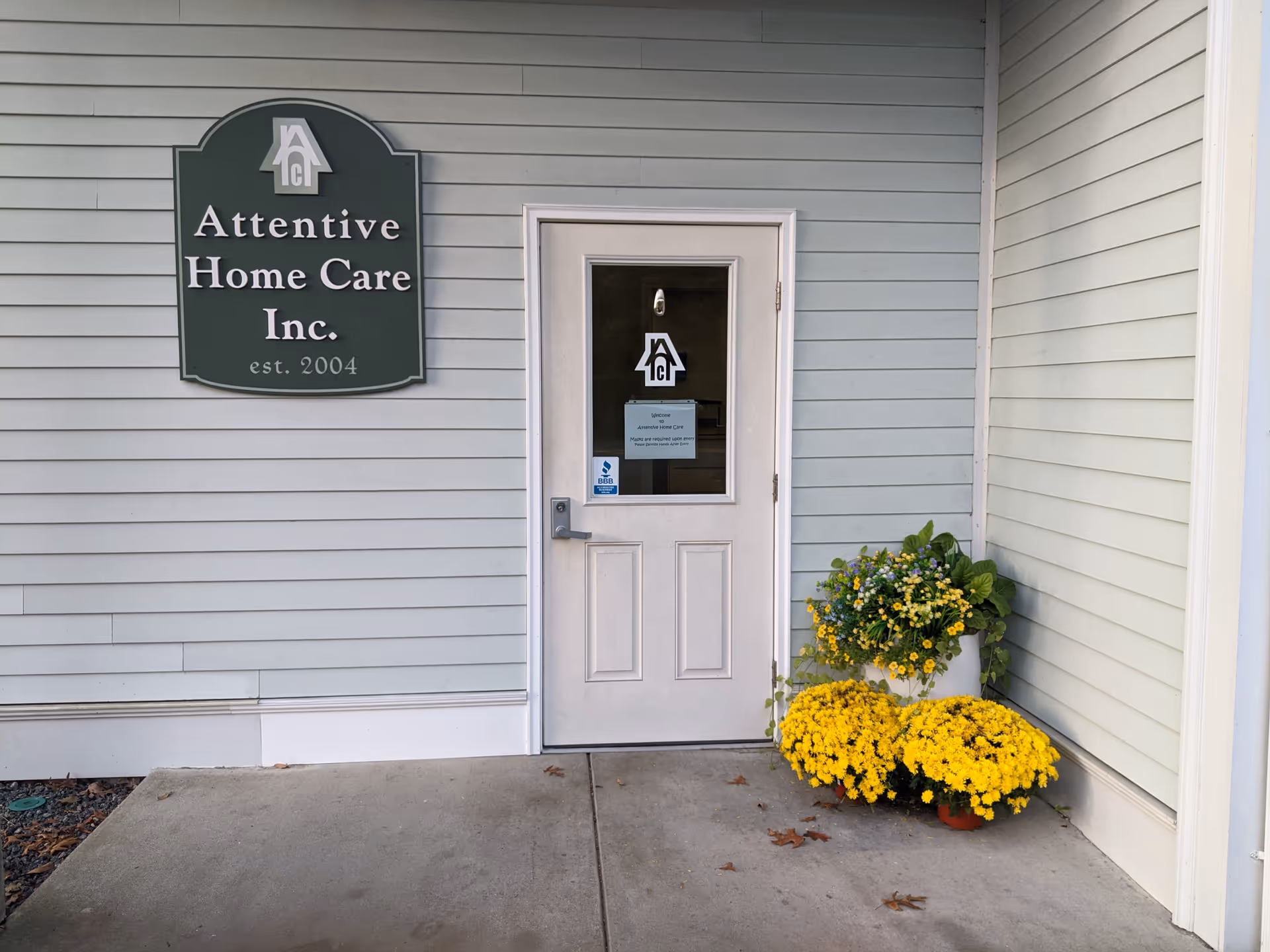 Front entrance of Attentive Home Care Inc. with sign and potted yellow flowers.