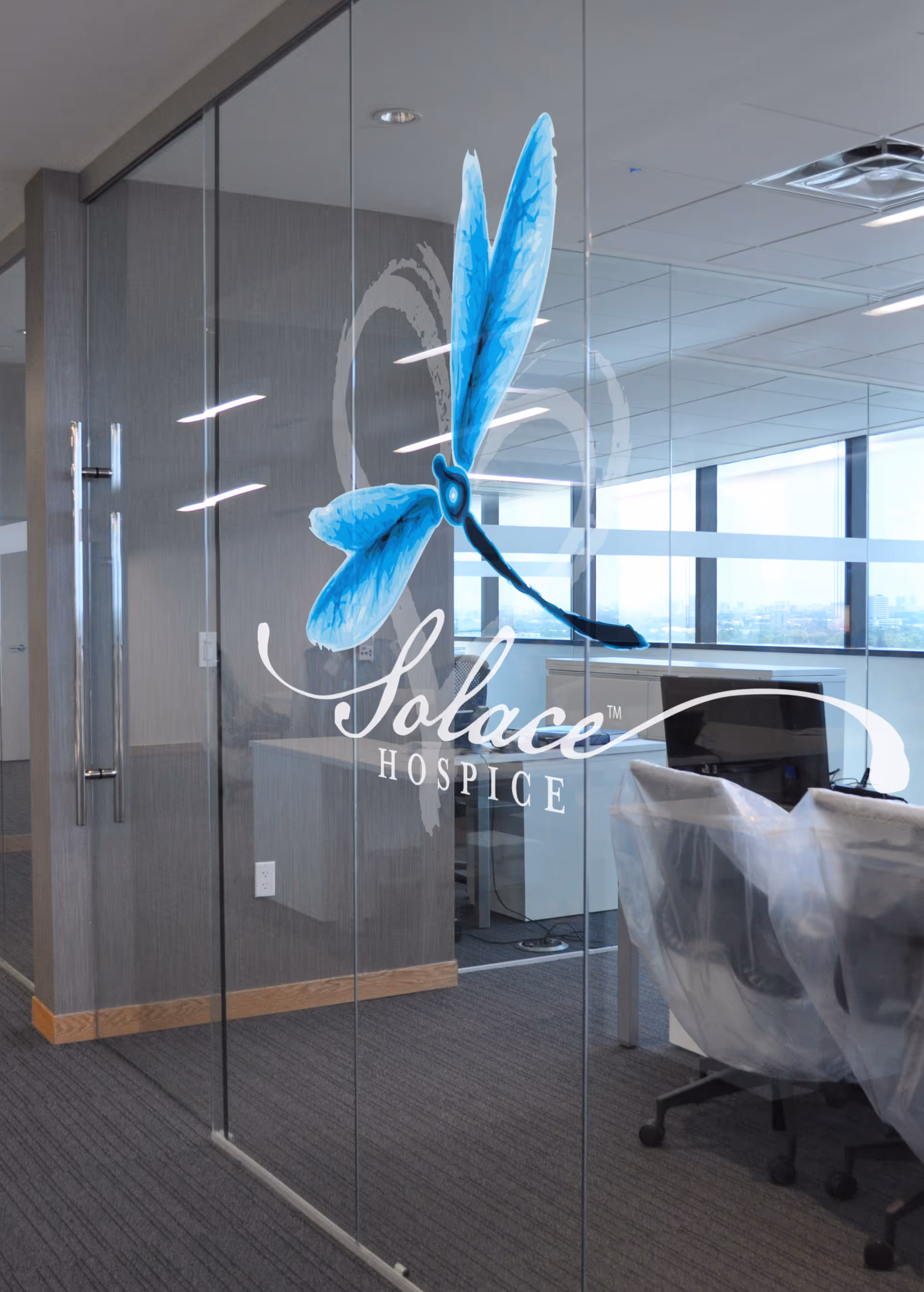 Glass conference room with Solace Hospice logo and blue dragonfly; office chairs visible behind.