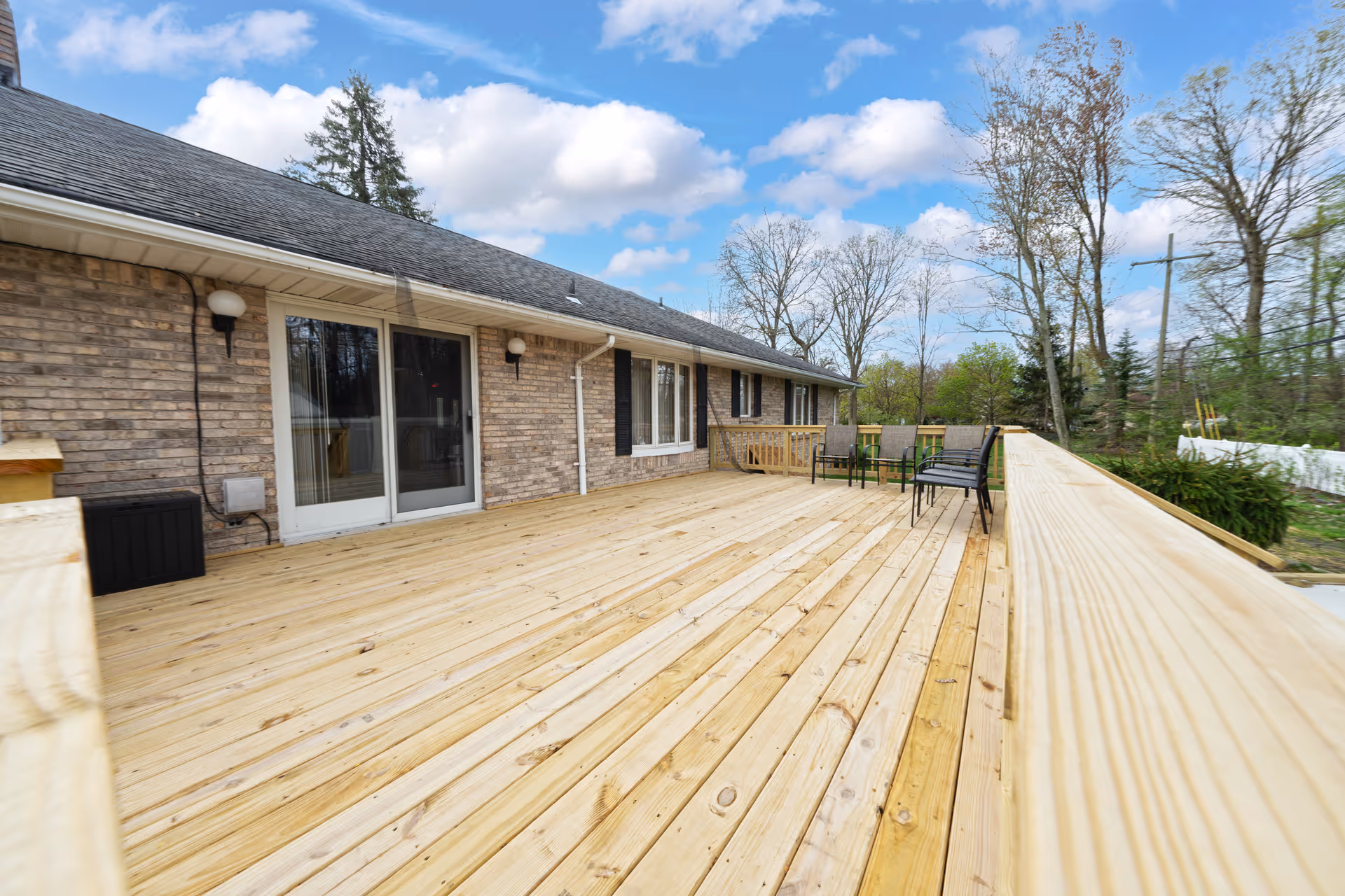 Wide wooden deck alongside brick building with sliding doors and outdoor seating.