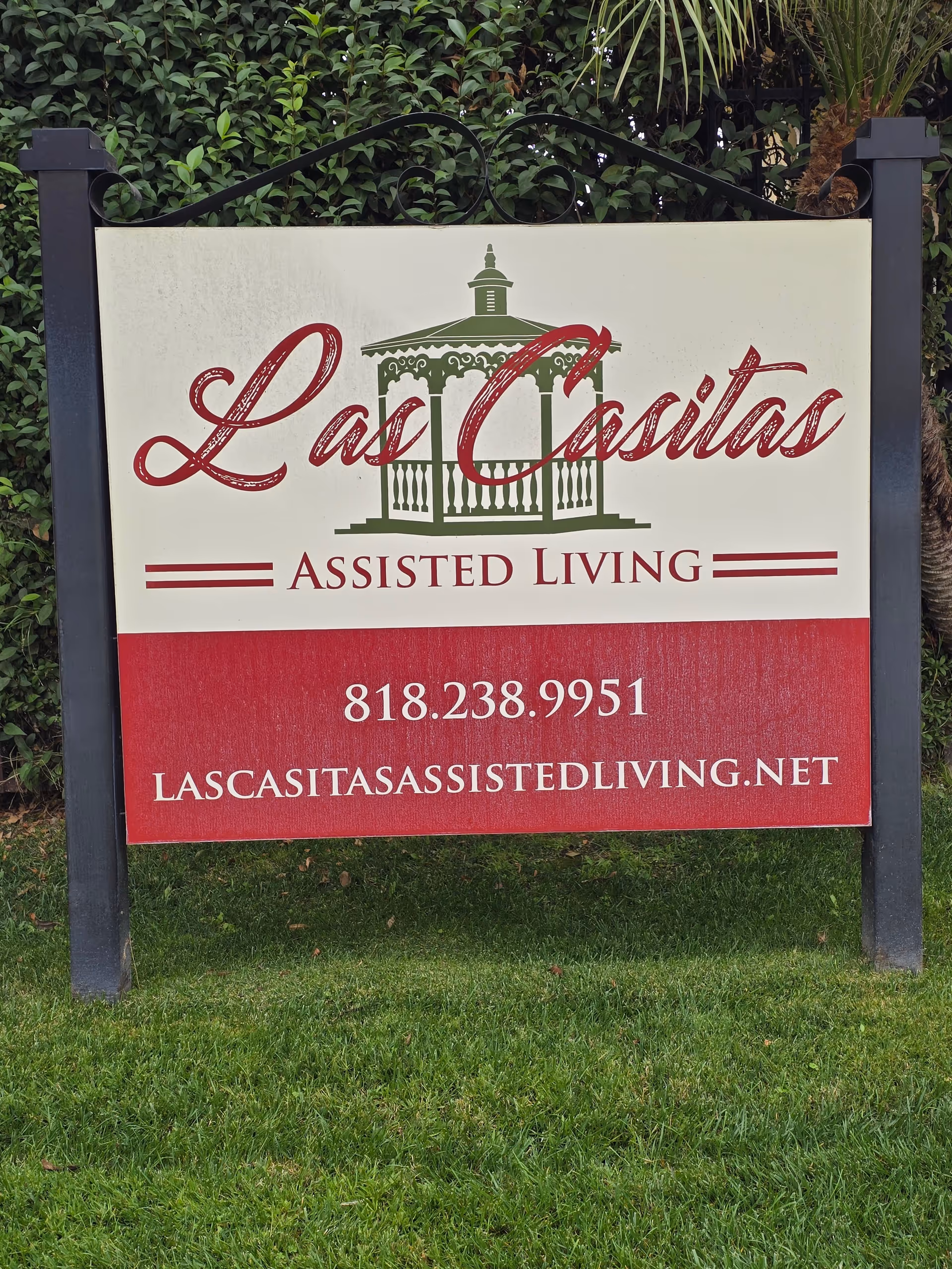 Outdoor sign for Las Casitas Assisted Living with hedges and posts.