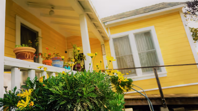 Exterior of Abiding Care facility, a yellow house with porch, potted plants, and white railing.