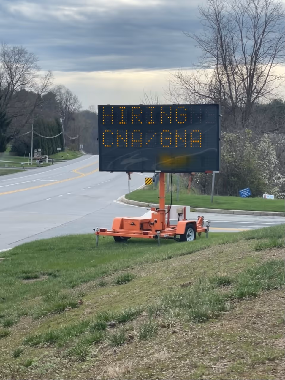 Portable roadside LED sign on an orange trailer beside a grassy slope.