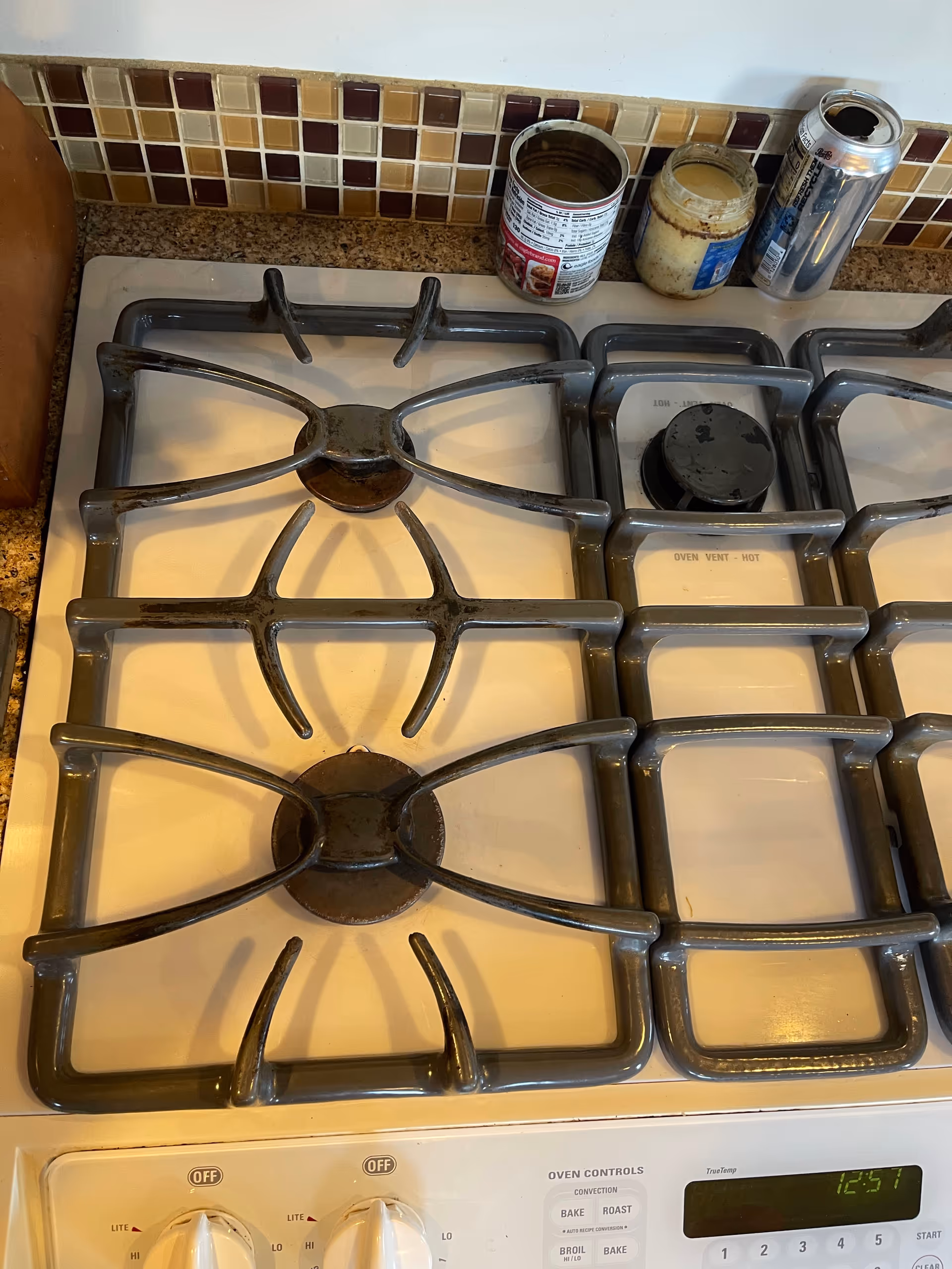 Gas stove with four burners and jars on a tiled kitchen counter.