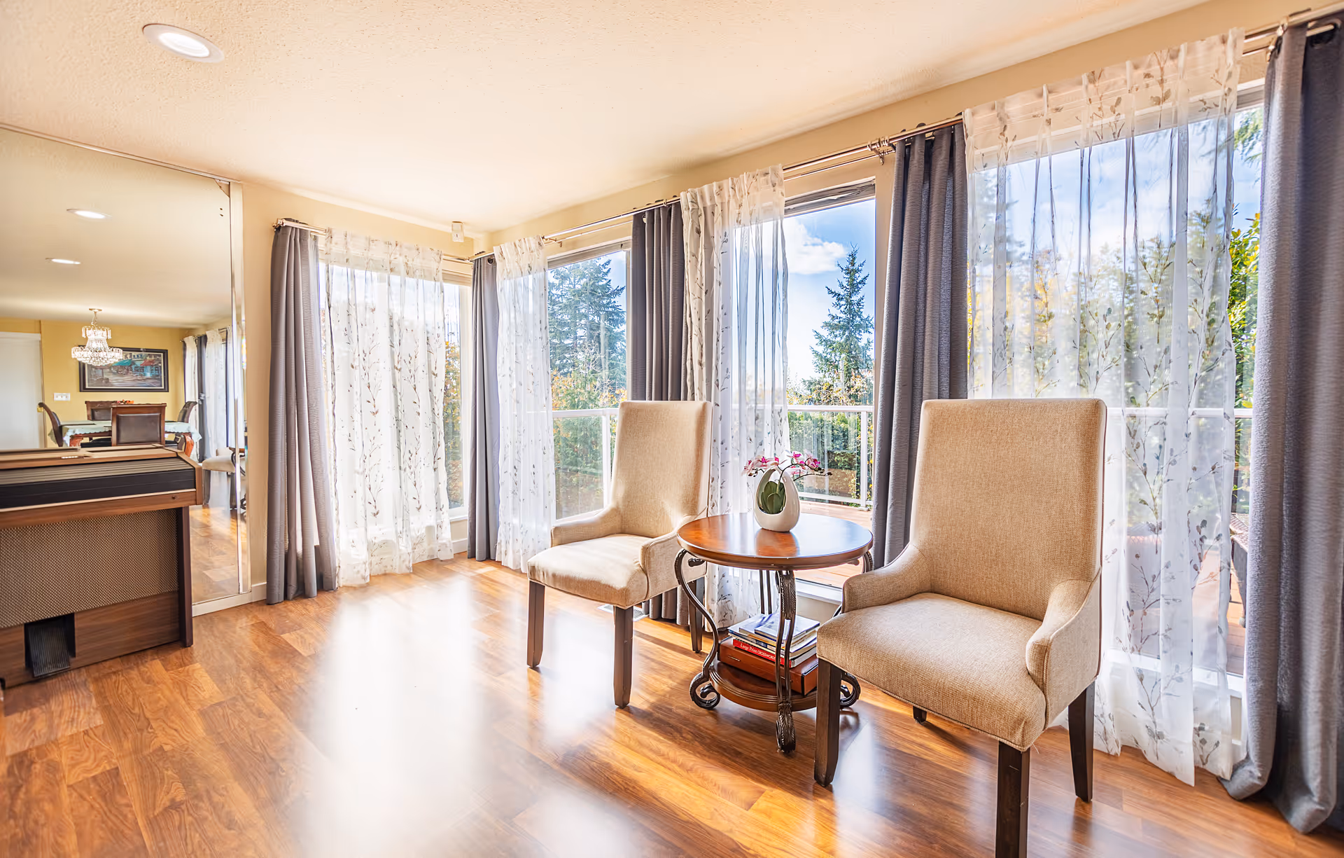 Bright living room with two beige chairs, a round table, and large windows.