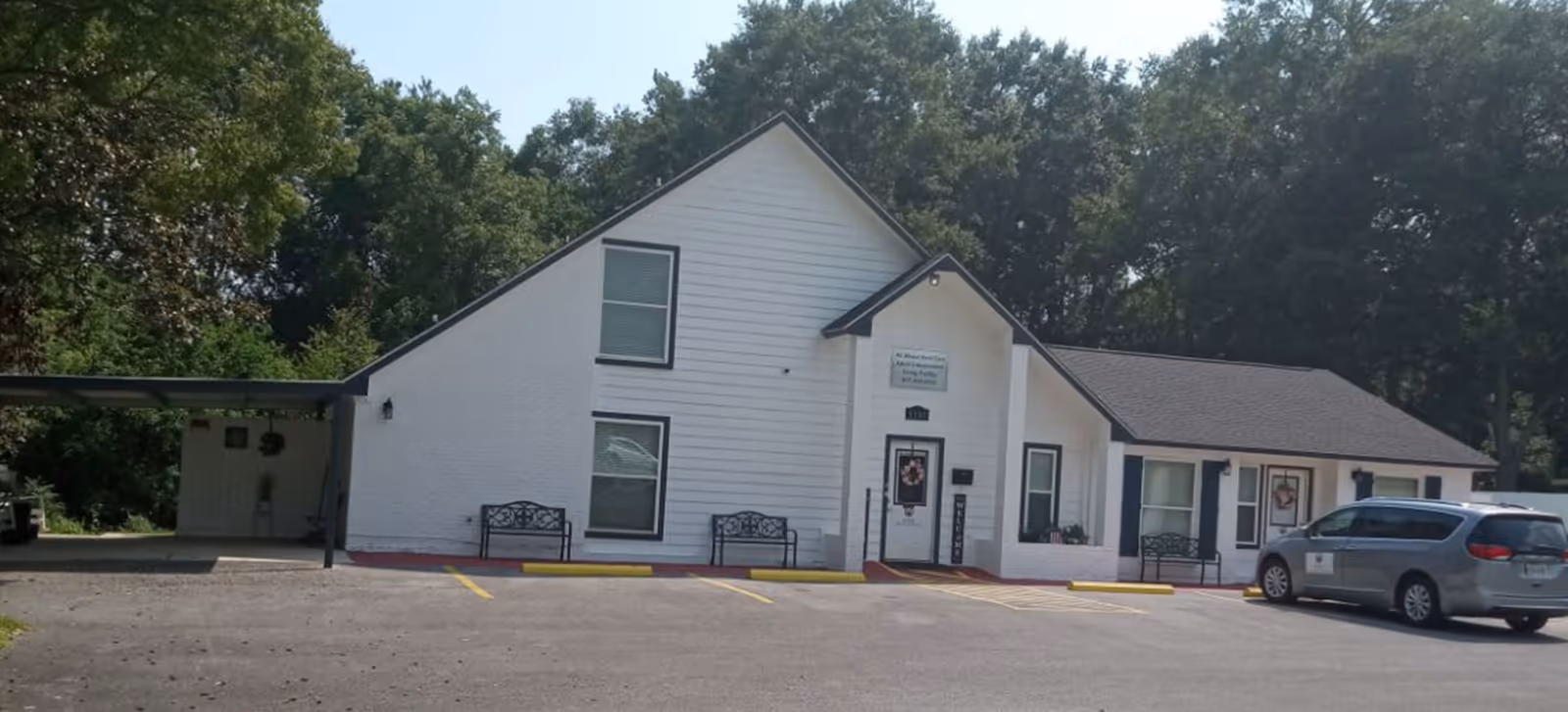 White senior care facility exterior with benches, parking lot, and a parked minivan.