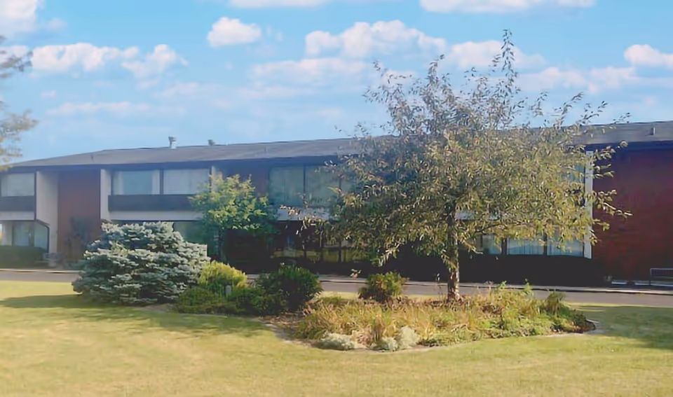 A senior living facility exterior with a landscaped yard and trees.