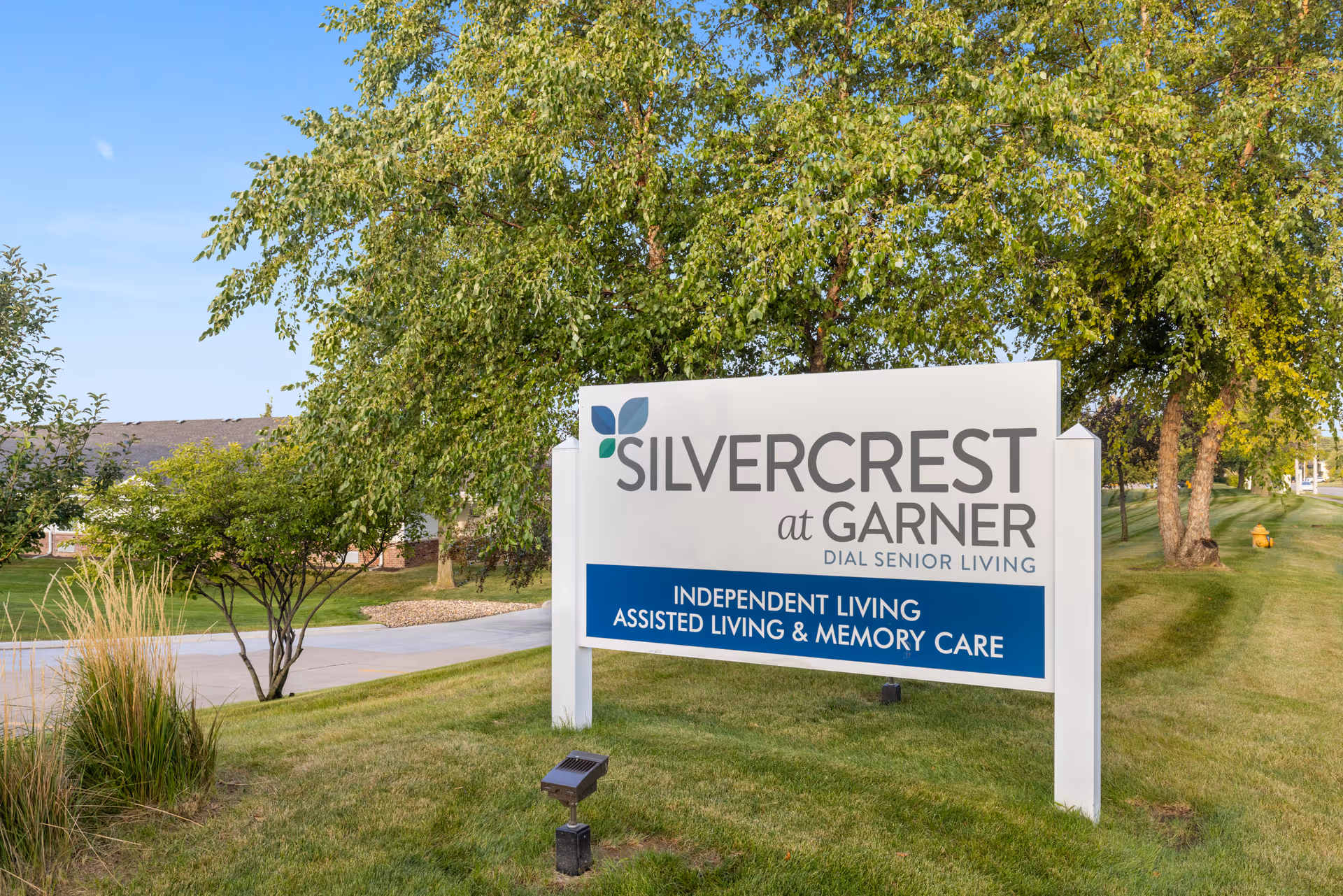 A large Silvercrest at Garner senior living sign on a grassy lawn with trees and a building in the background.