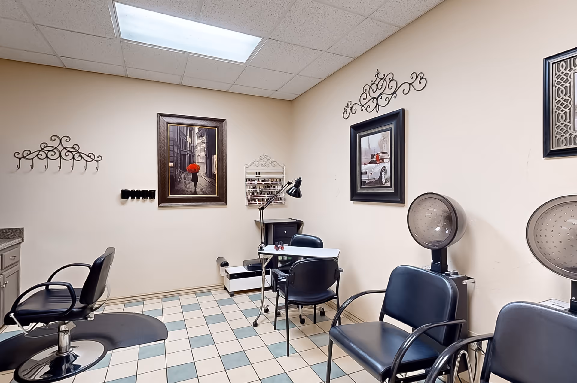 Interior senior living salon with chairs, dryers, and framed art on beige walls.