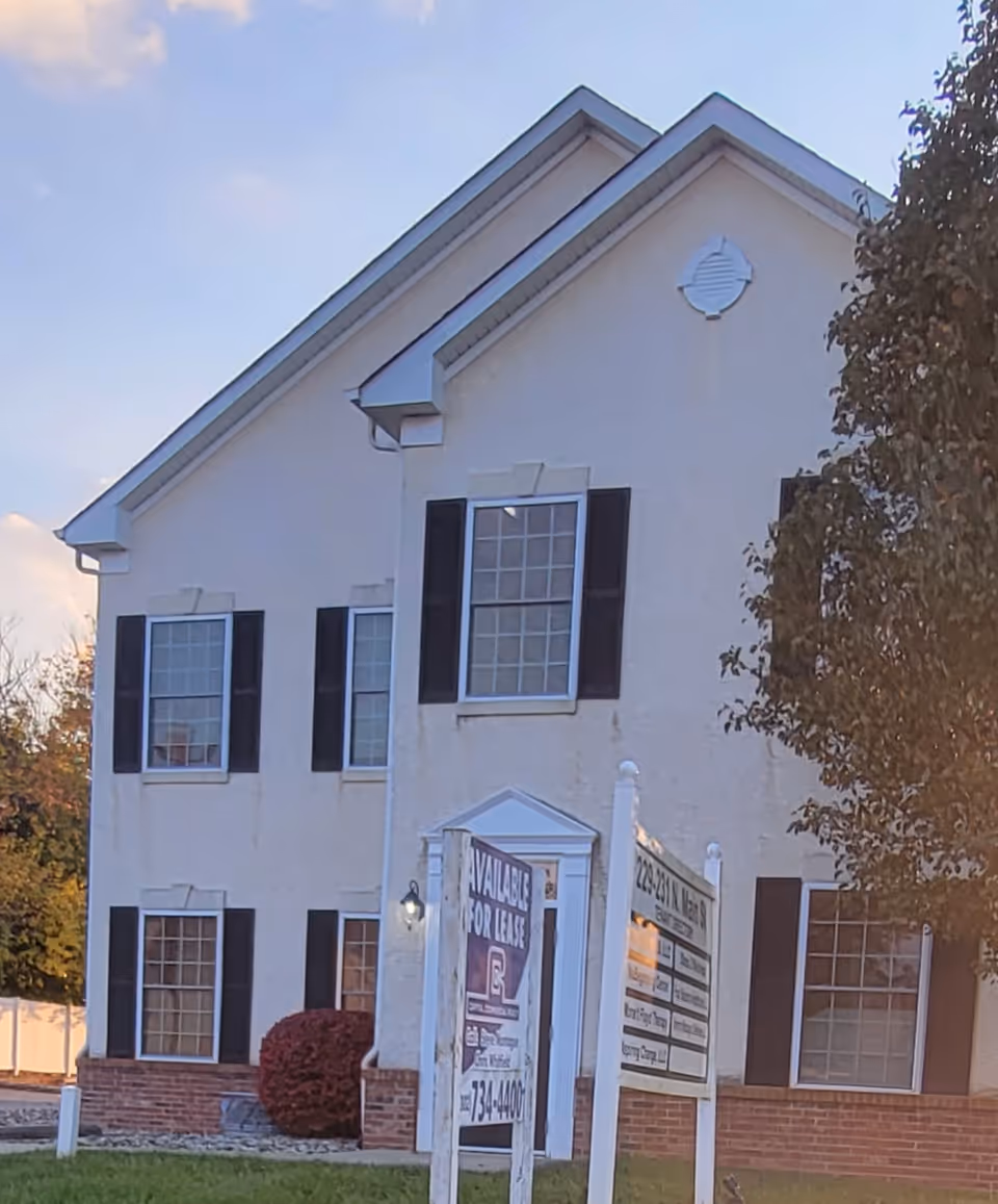 White two-story senior living facility exterior with black shutters and a front sign