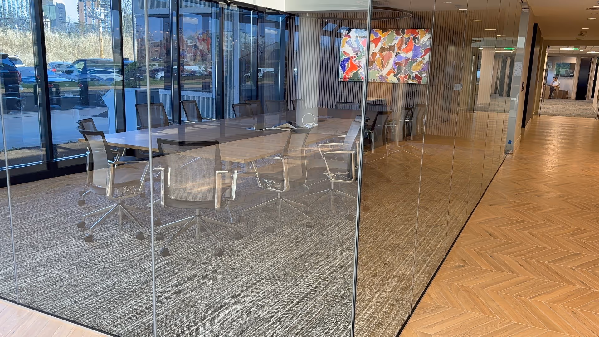 Glass-walled conference room with a long table and office chairs in a modern facility hallway.