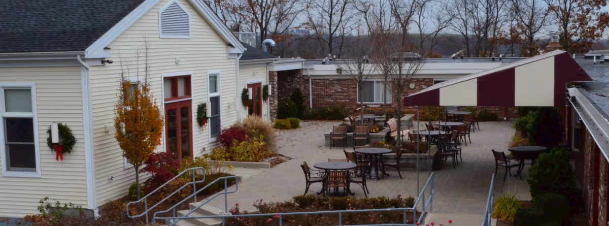 Outdoor courtyard patio between single-story buildings with tables, chairs, a striped canopy, and holiday wreaths on the walls.