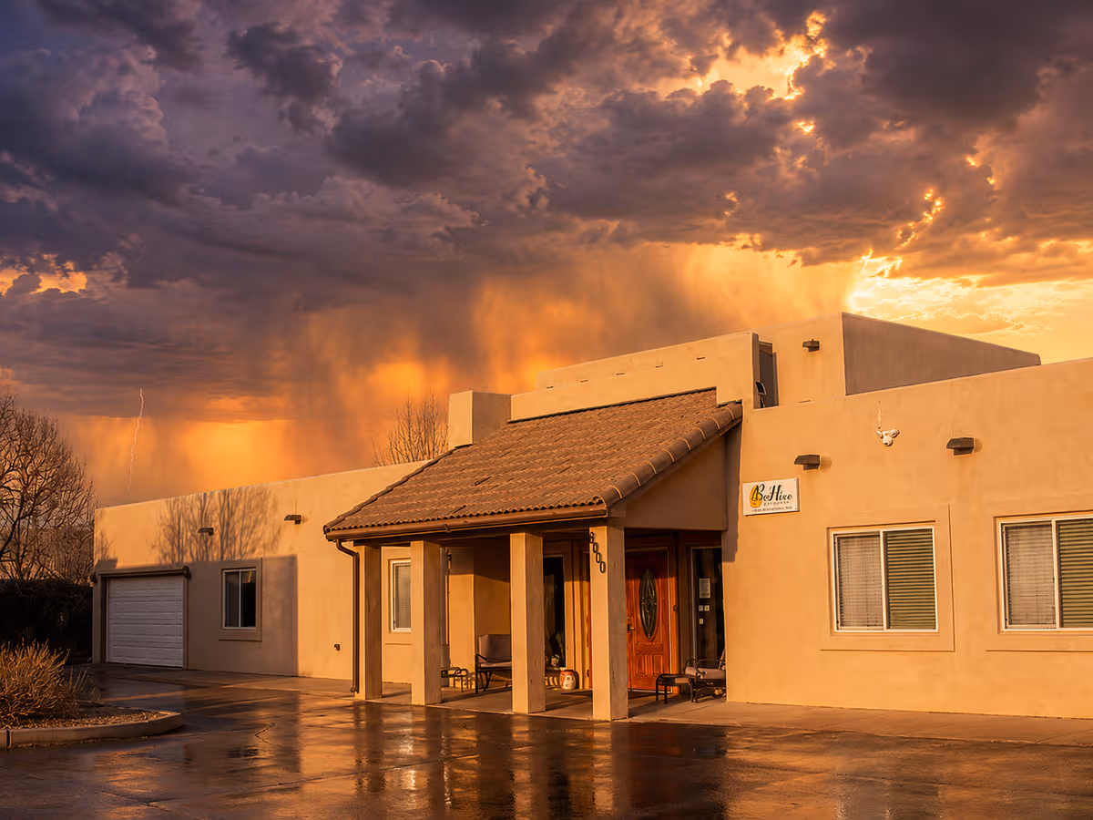BeeHive Homes Albuquerque West exterior with stucco walls and dramatic stormy sunset