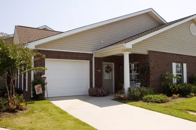 Brick senior living facility exterior featuring a white garage, covered front porch, and landscaping.