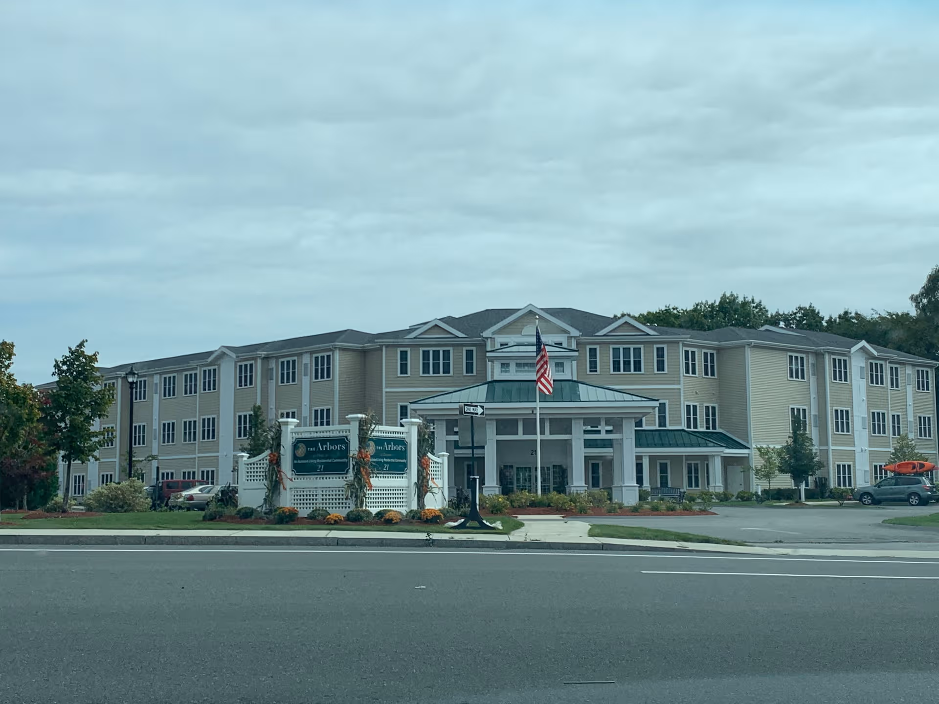 Exterior view of The Arbors at Dracut senior living with entrance and American flag.
