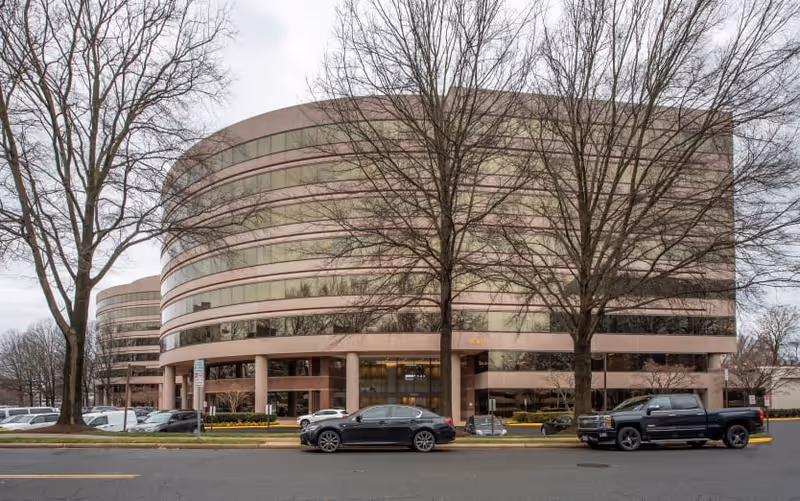 Exterior view of a curved, multi-story building with parked cars and leafless trees.