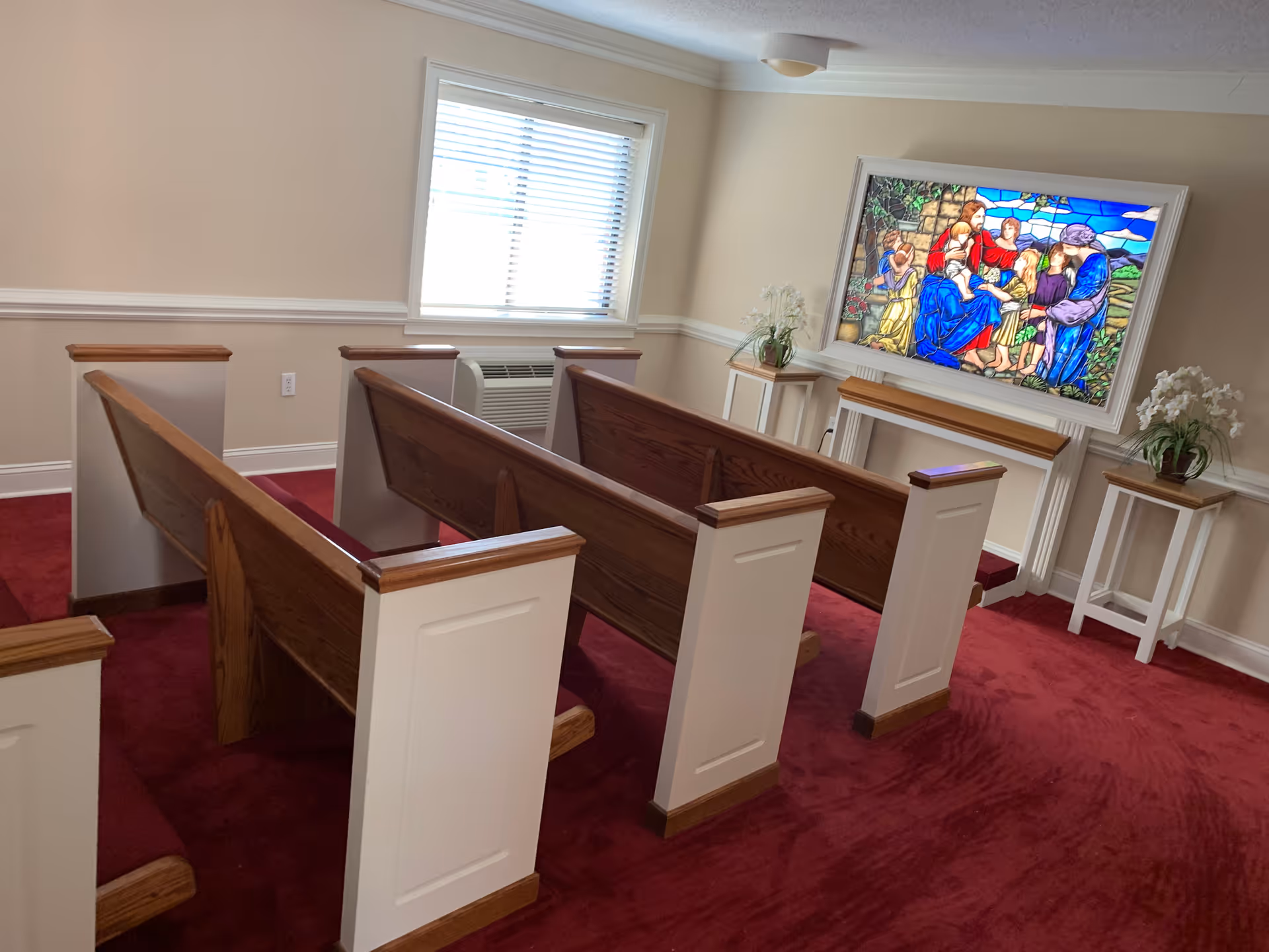 Interior chapel with wooden pews, red carpet, and stained glass window.