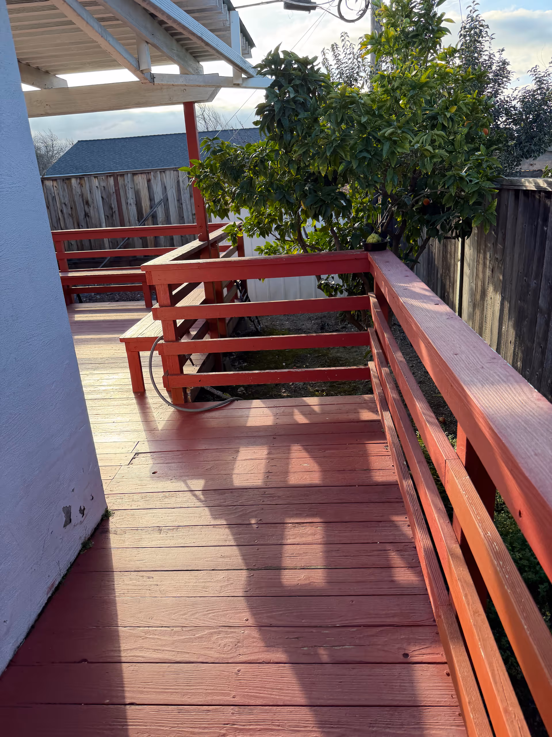 Red wooden deck with railing beside a tree and fence outside a residential building