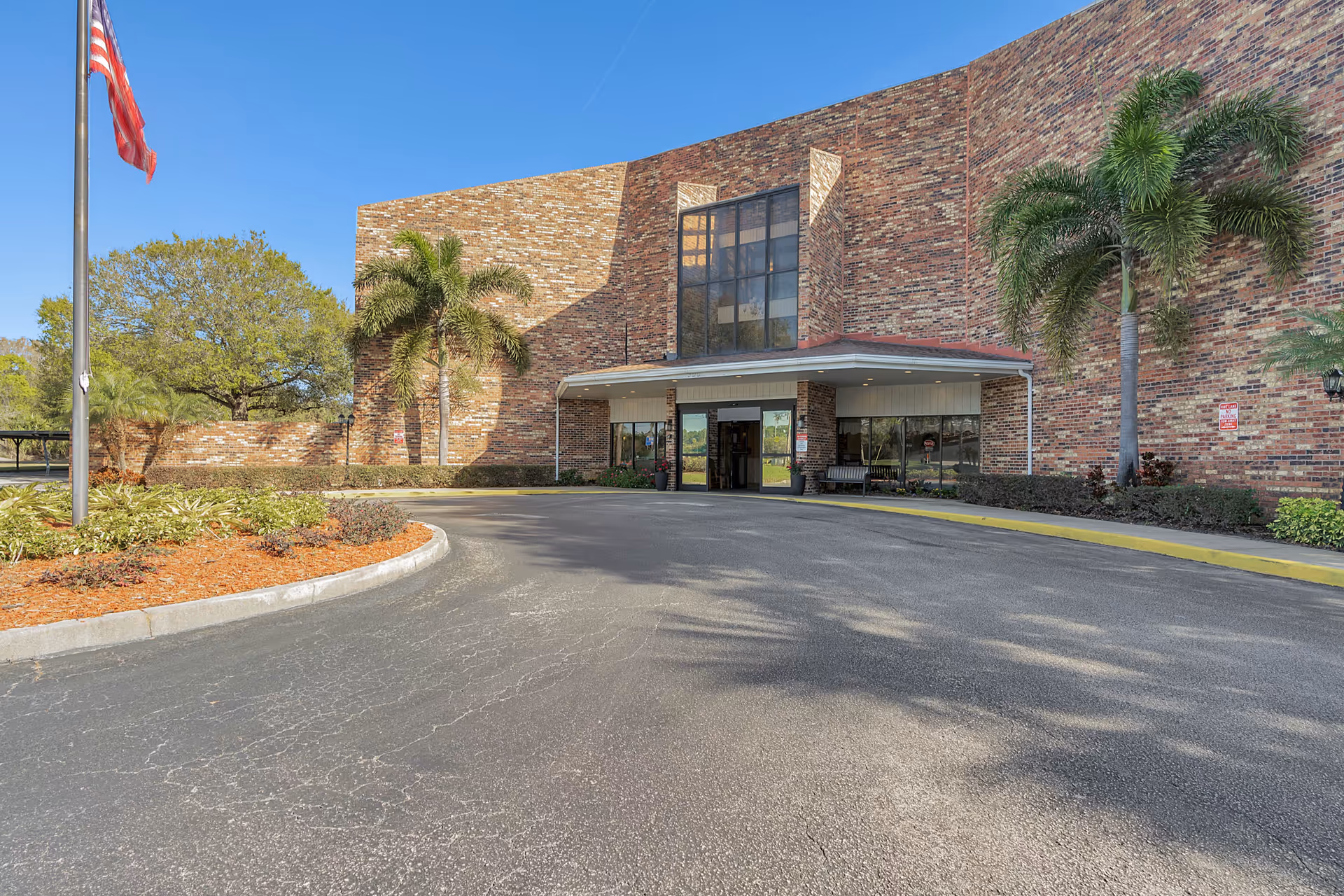 Exterior view of a brick senior living facility with a covered entrance and palm trees.