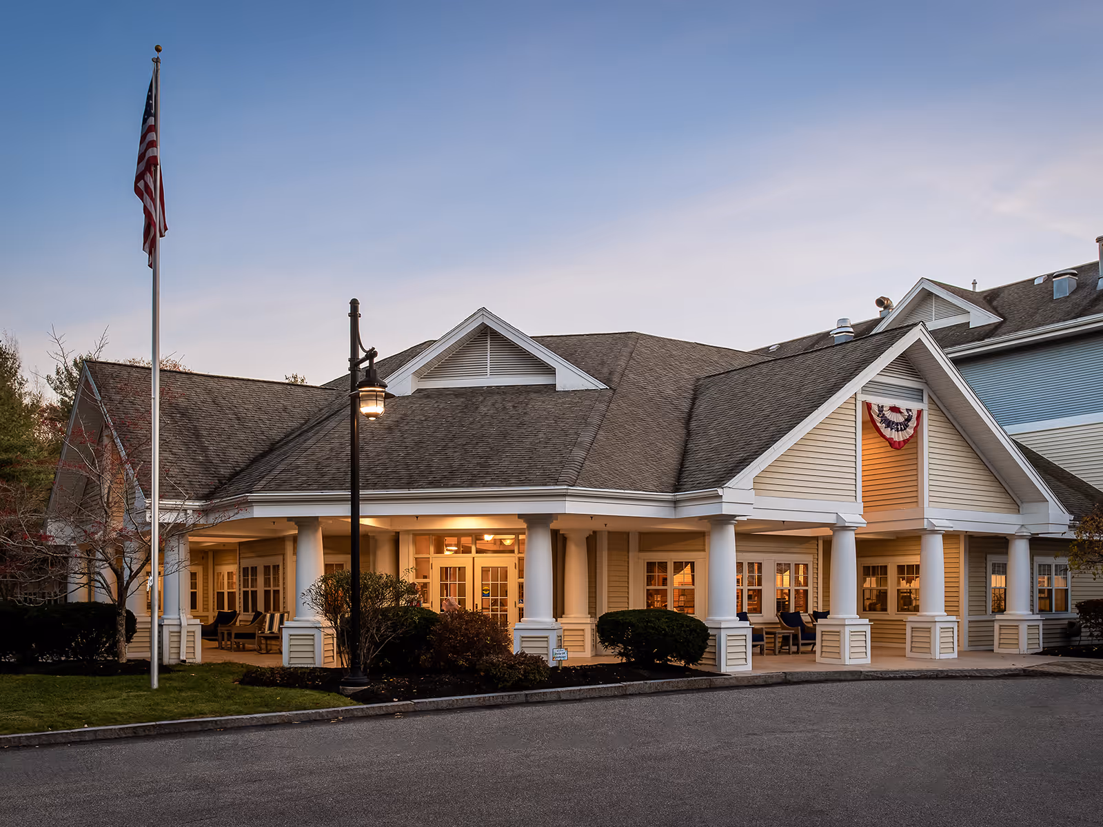 Atria Kennebunk facility front exterior with a flag and welcoming porch.