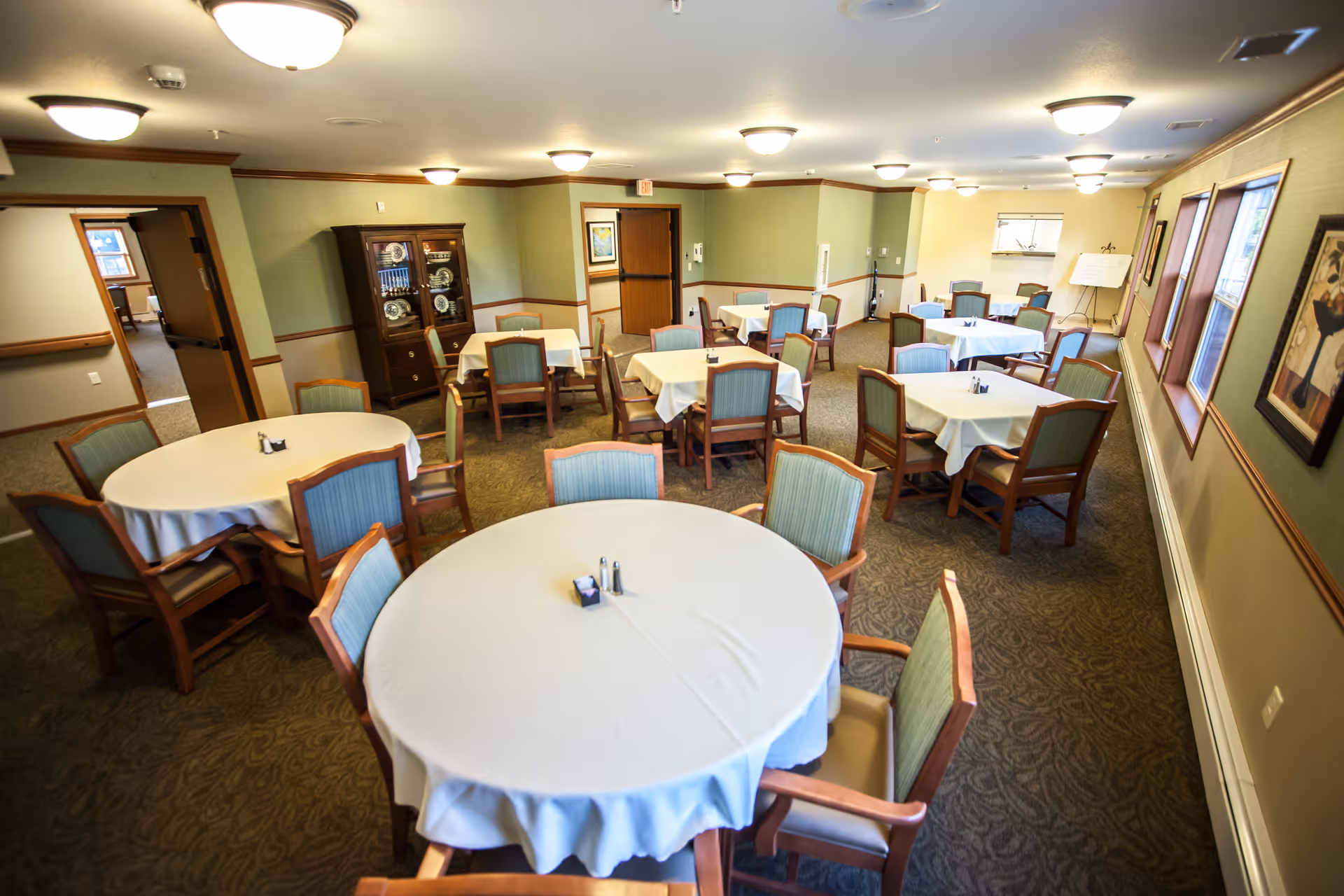 Dining room with multiple round tables covered in white tablecloths and wooden chairs.