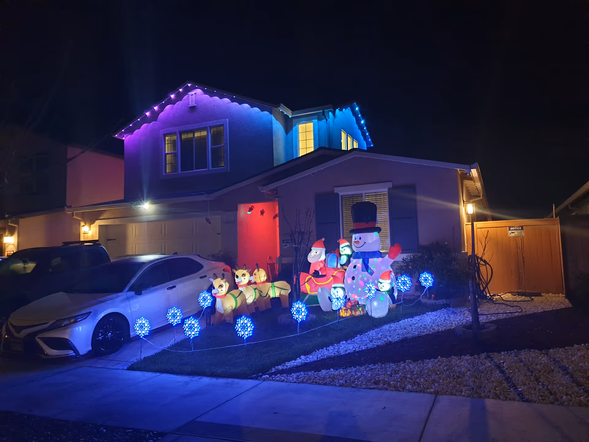 Night exterior of a house decorated with colorful holiday lights and inflatables.