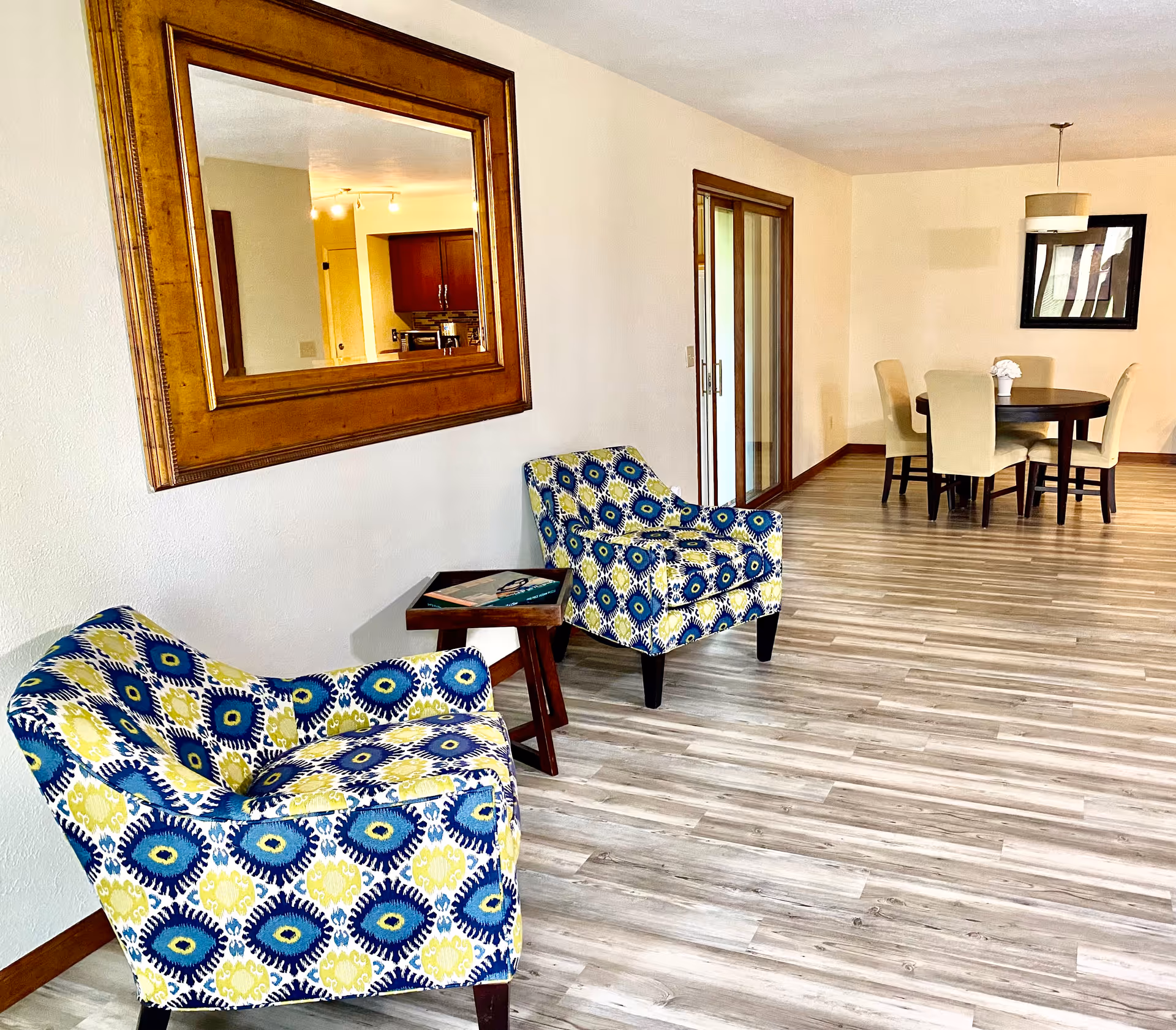Bright living area with patterned armchairs, a mirror, and a dining nook in background.