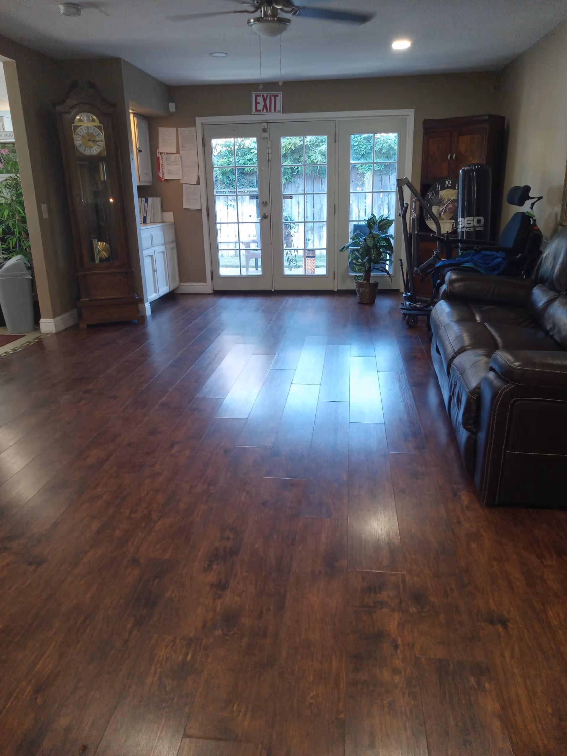 Interior living room with dark wood floors, sofa, grandfather clock, and exit doors.