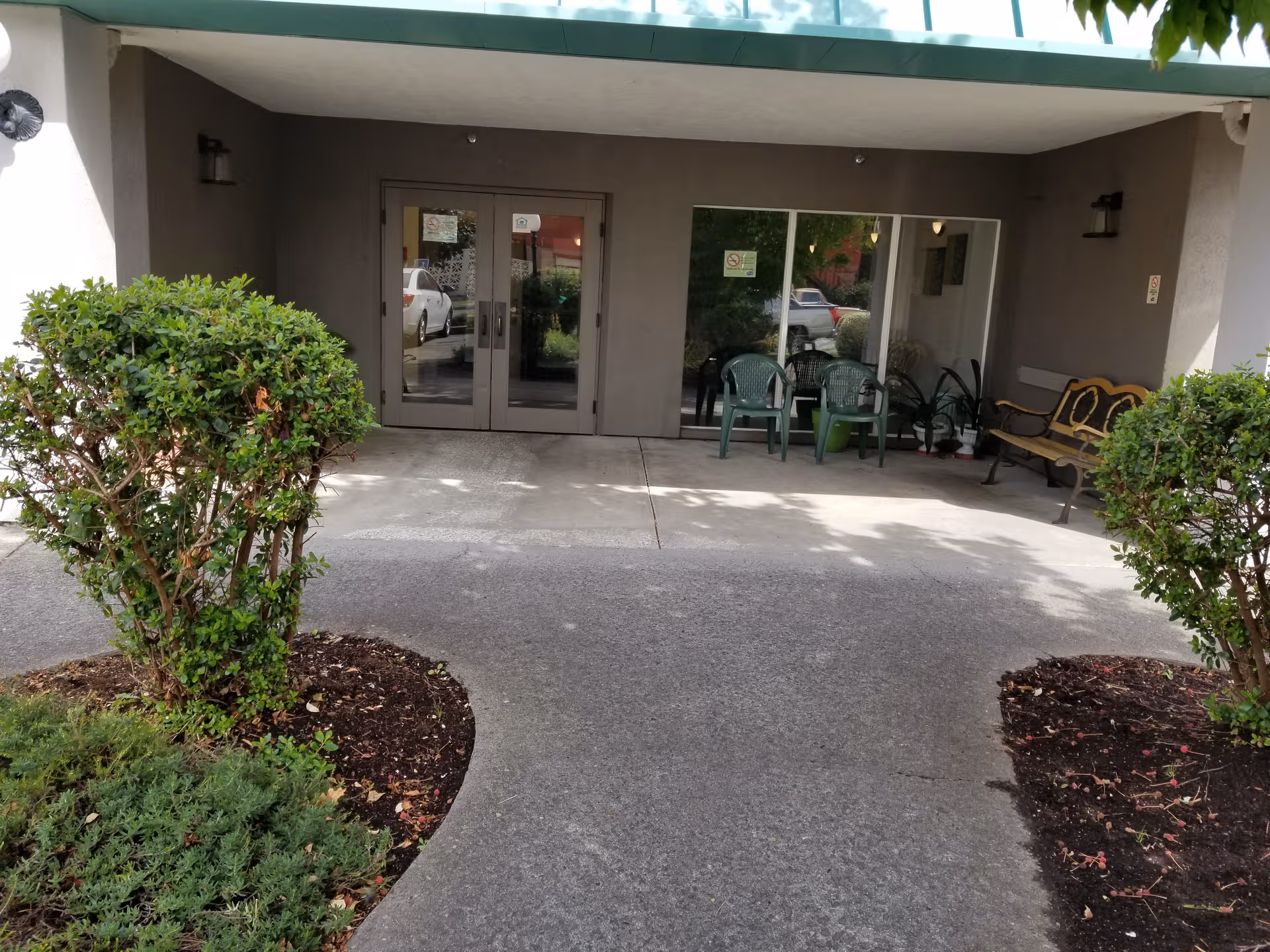 Entrance to Hemlock Court, glass doors under a covered walkway with green chairs outside.