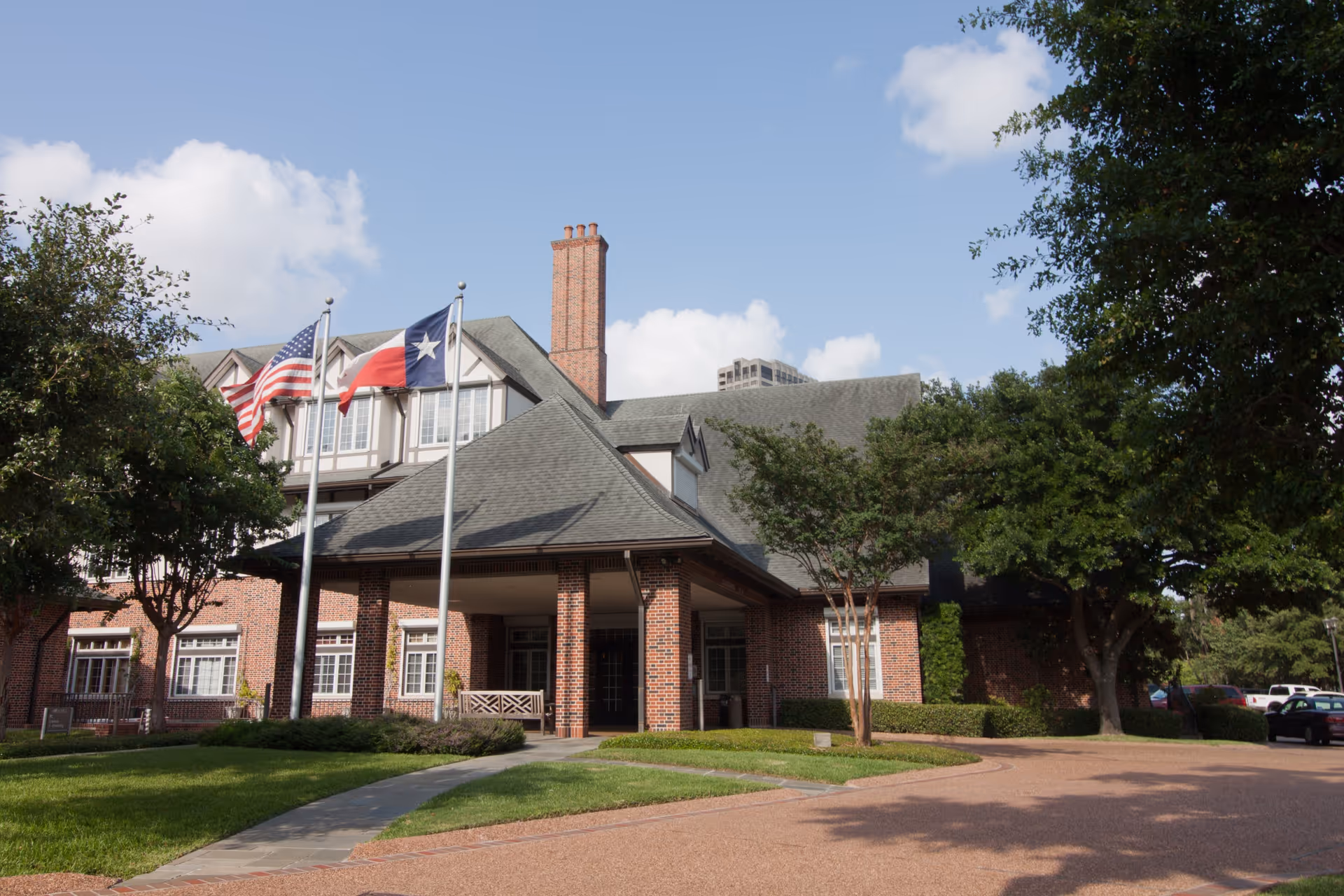 Brick Houston Hospice building with flags, a columned entrance, and manicured lawn on a sunny day.