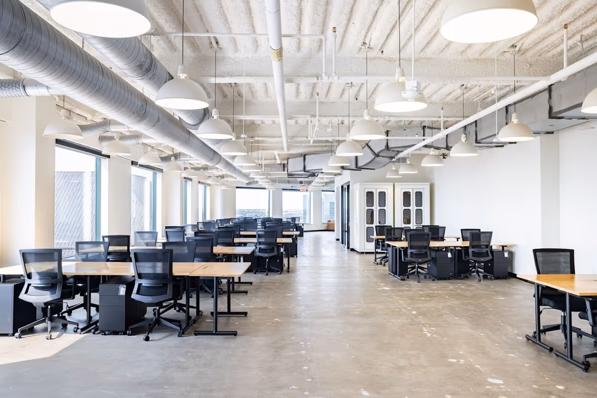 A spacious, modern open-plan interior with rows of desks and black office chairs.