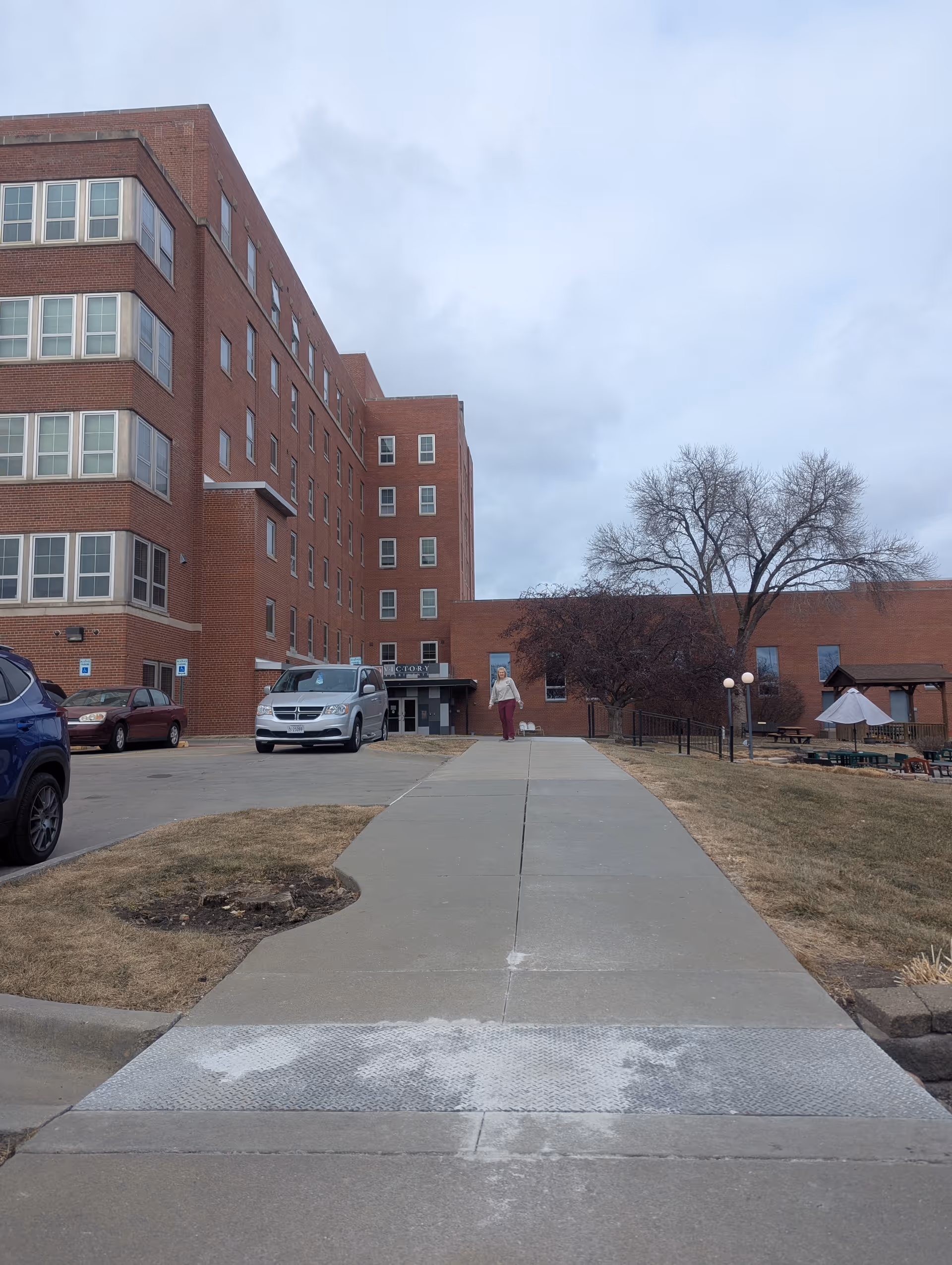 Brick senior living building with a curved walkway and parked cars leading to the entrance.