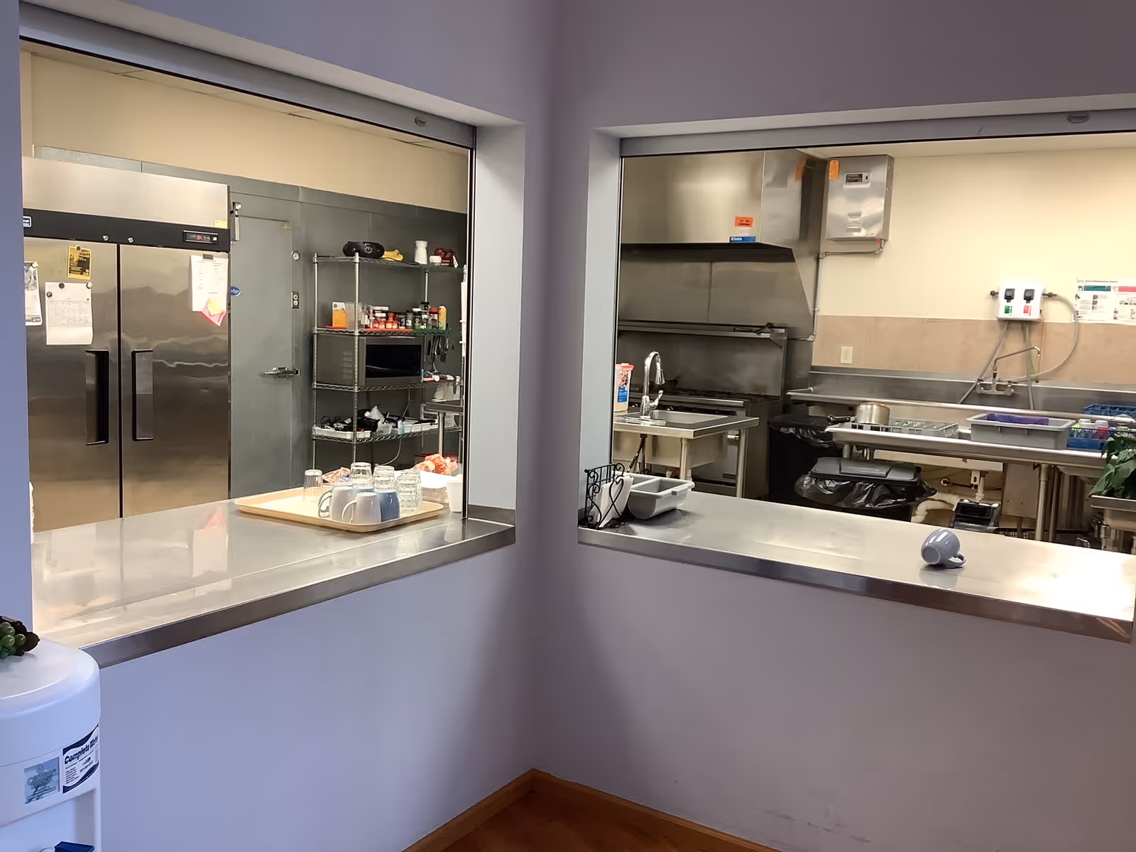 Two pass-through windows reveal a stainless-steel kitchen with appliances, shelves, and prep area.