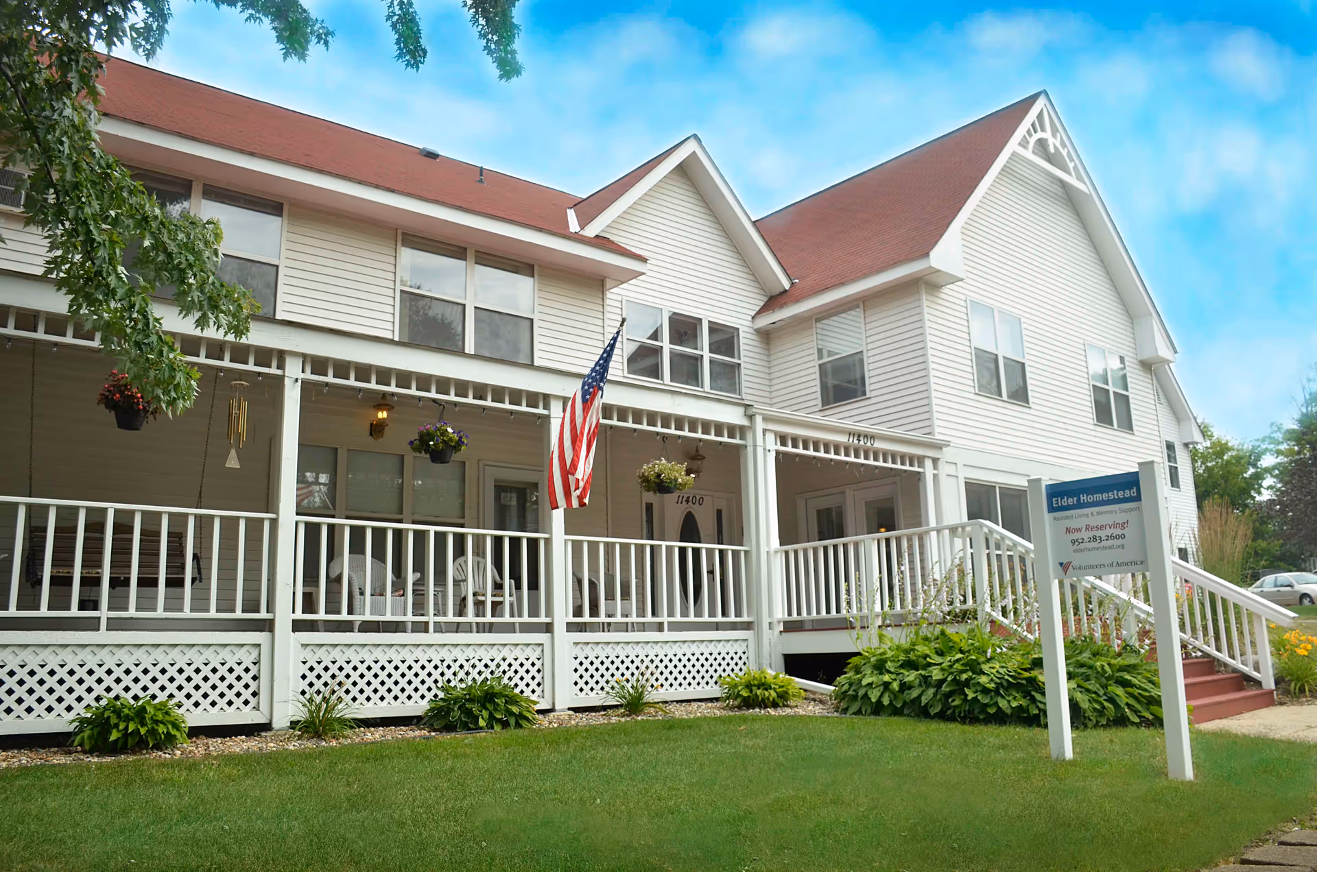 White two-story senior living facility with a wraparound porch and American flag.