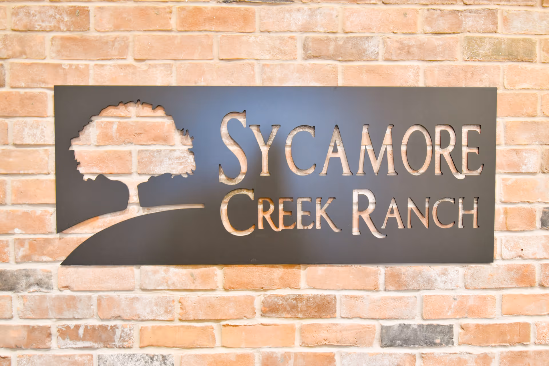 Metal sign reading Sycamore Creek Ranch mounted on a brick exterior wall.