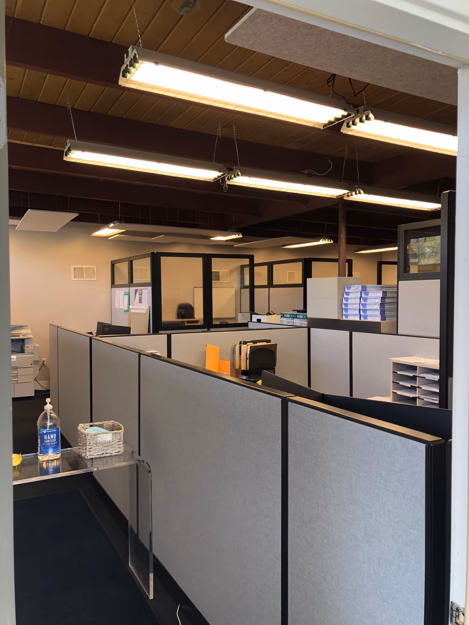 Office cubicles and desks in a facility's administrative area with fluorescent lighting.