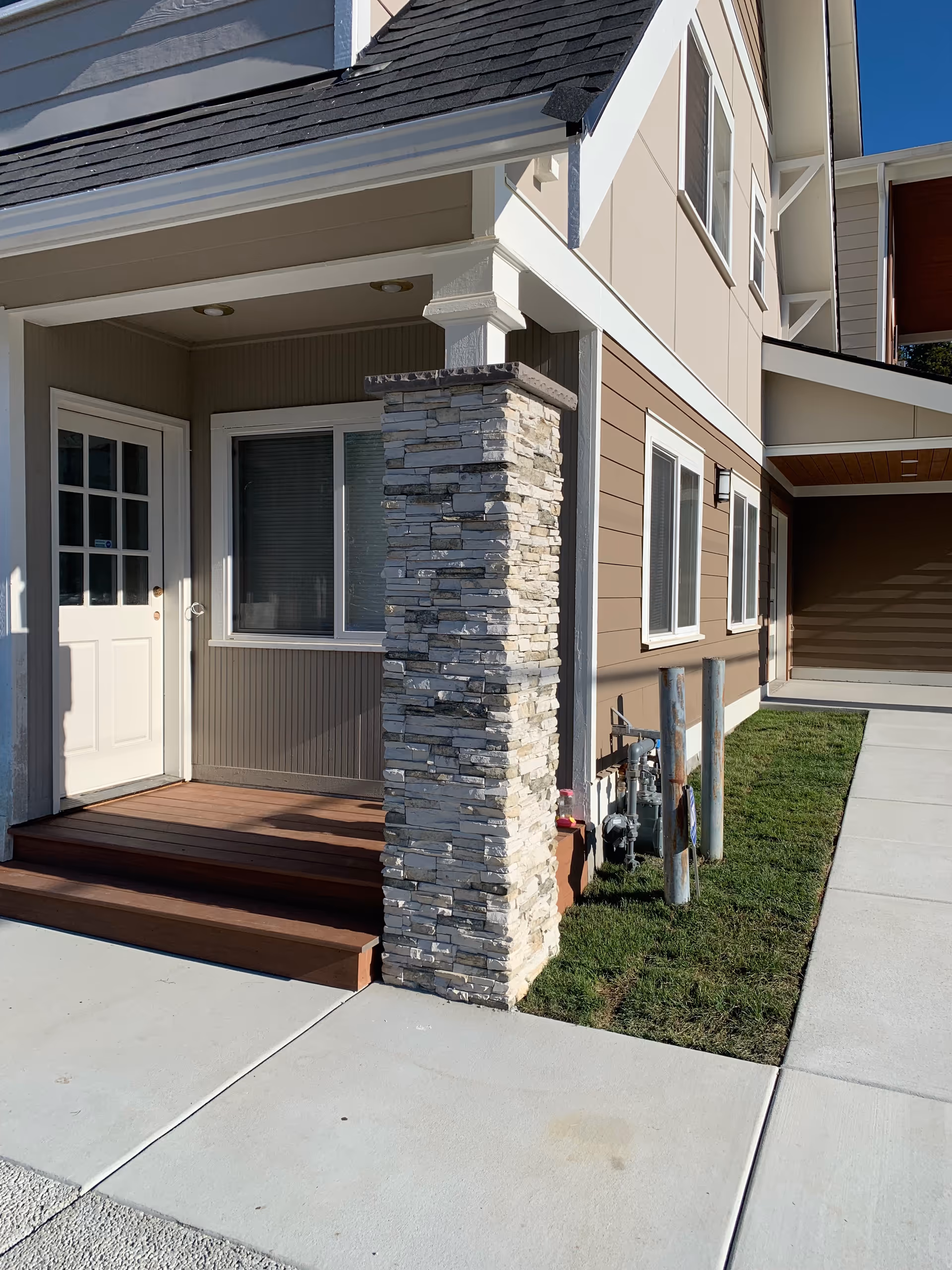Beige senior living building entrance with stone pillar, porch, and steps.
